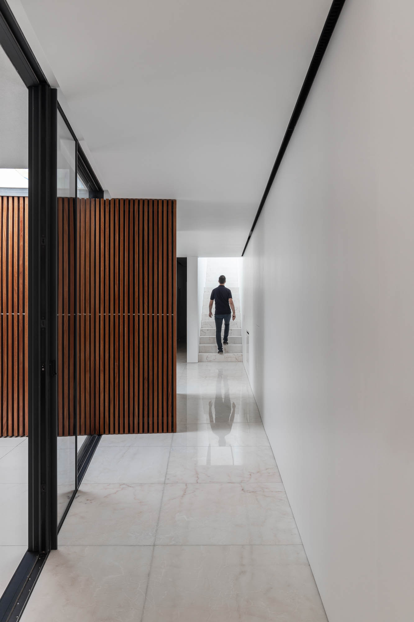Corredor: Pavimento em mármore, paredes brancas, porta de madeira ripada e vista para escadas. Design moderno e elegante. — Casa Costa Nova arquitetura Espaço Objecto em Ílhavo