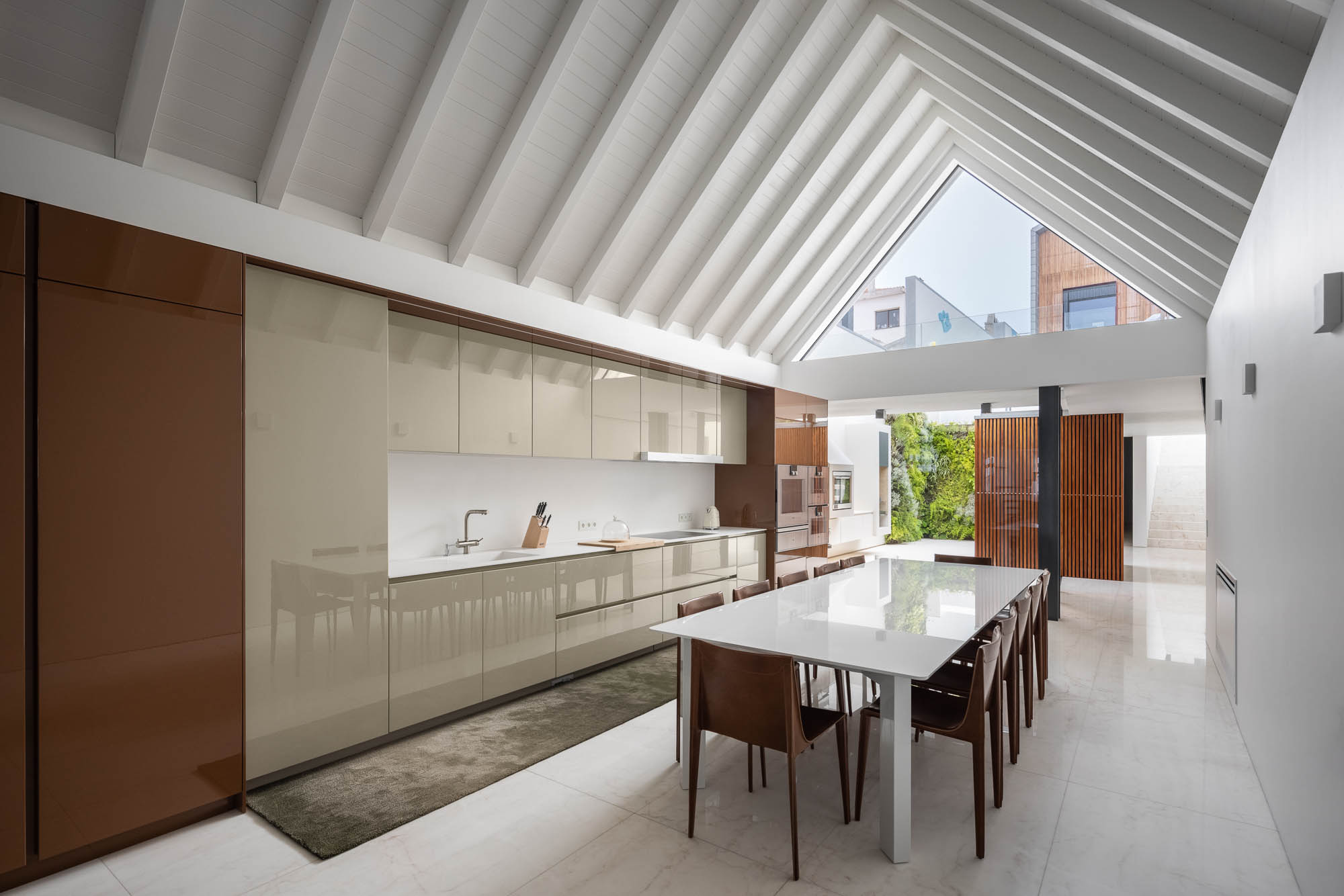 Cozinha: Armários lacados em tons neutros, mesa branca com cadeiras de couro e vista para o pátio. Design moderno e funcional. — Casa Costa Nova arquitetura Espaço Objecto em Ílhavo