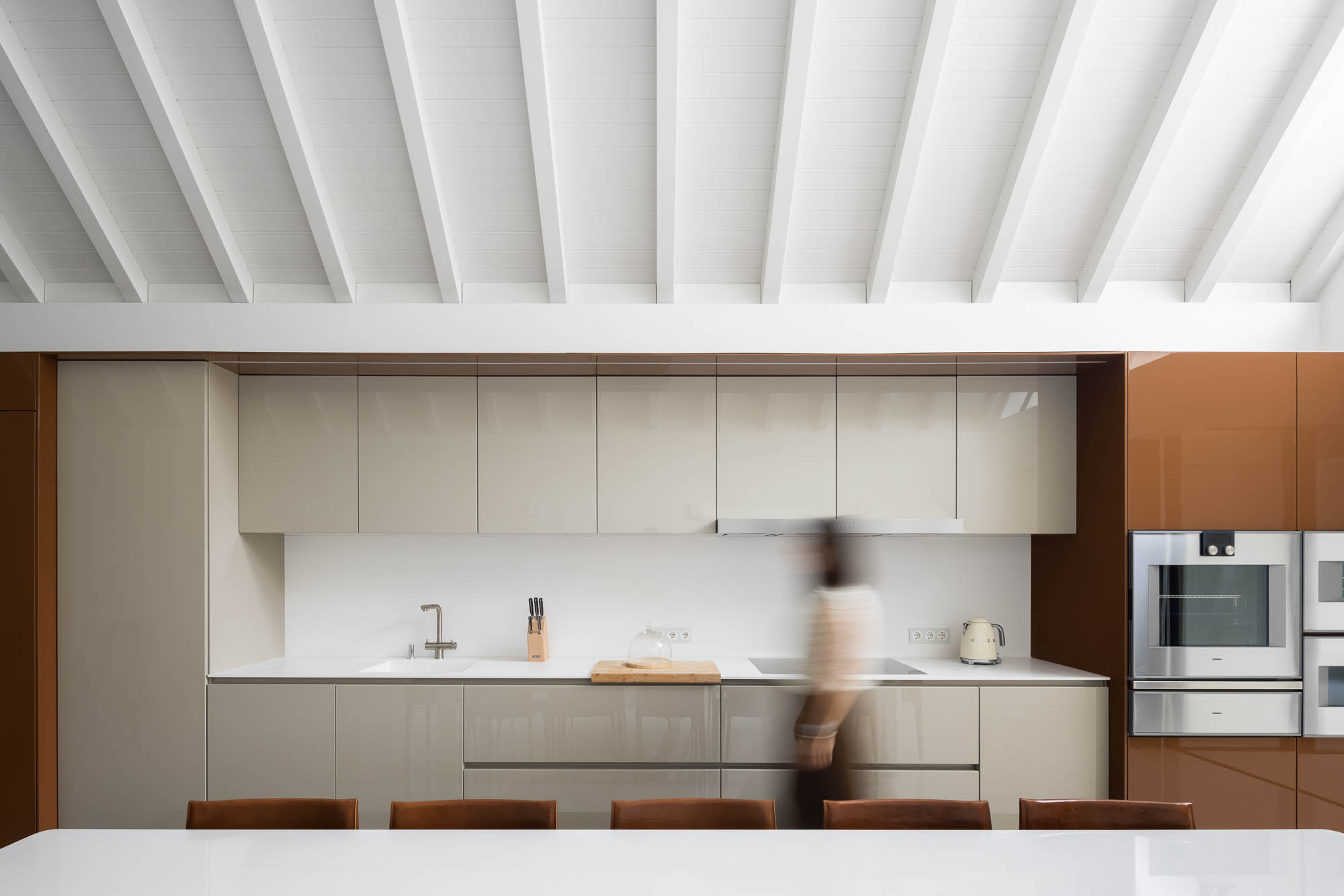 Cozinha: Armários lacados em tons neutros, bancada branca e eletrodomésticos em aço inoxidável. Espaço luminoso e minimalista. — Casa Costa Nova arquitetura Espaço Objecto em Ílhavo