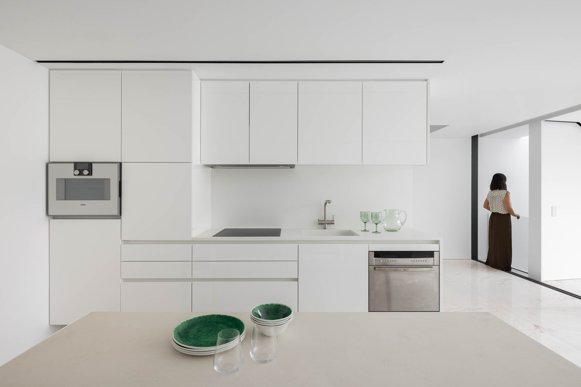 Cozinha: Armários brancos, bancada em pedra clara e eletrodomésticos modernos. Design clean e funcional. — Casa Costa Nova arquitetura Espaço Objecto em Ílhavo