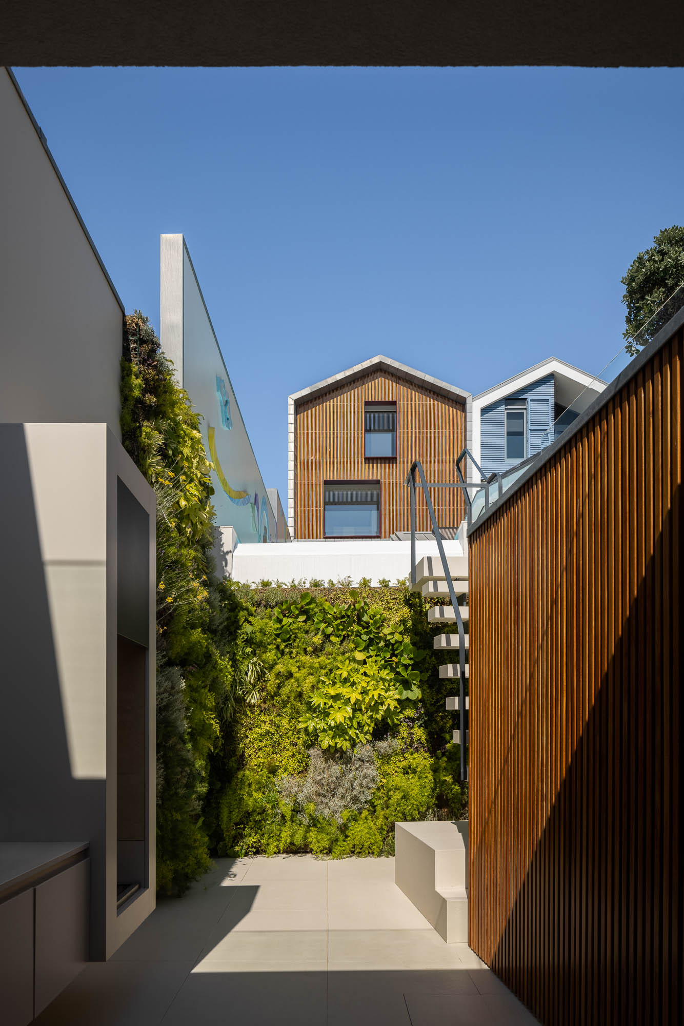Pátio: Parede verde vertical, revestimento em madeira e vista para as casas típicas da Costa Nova. Integração da arquitetura com a natureza. — Casa Costa Nova arquitetura Espaço Objecto em Ílhavo