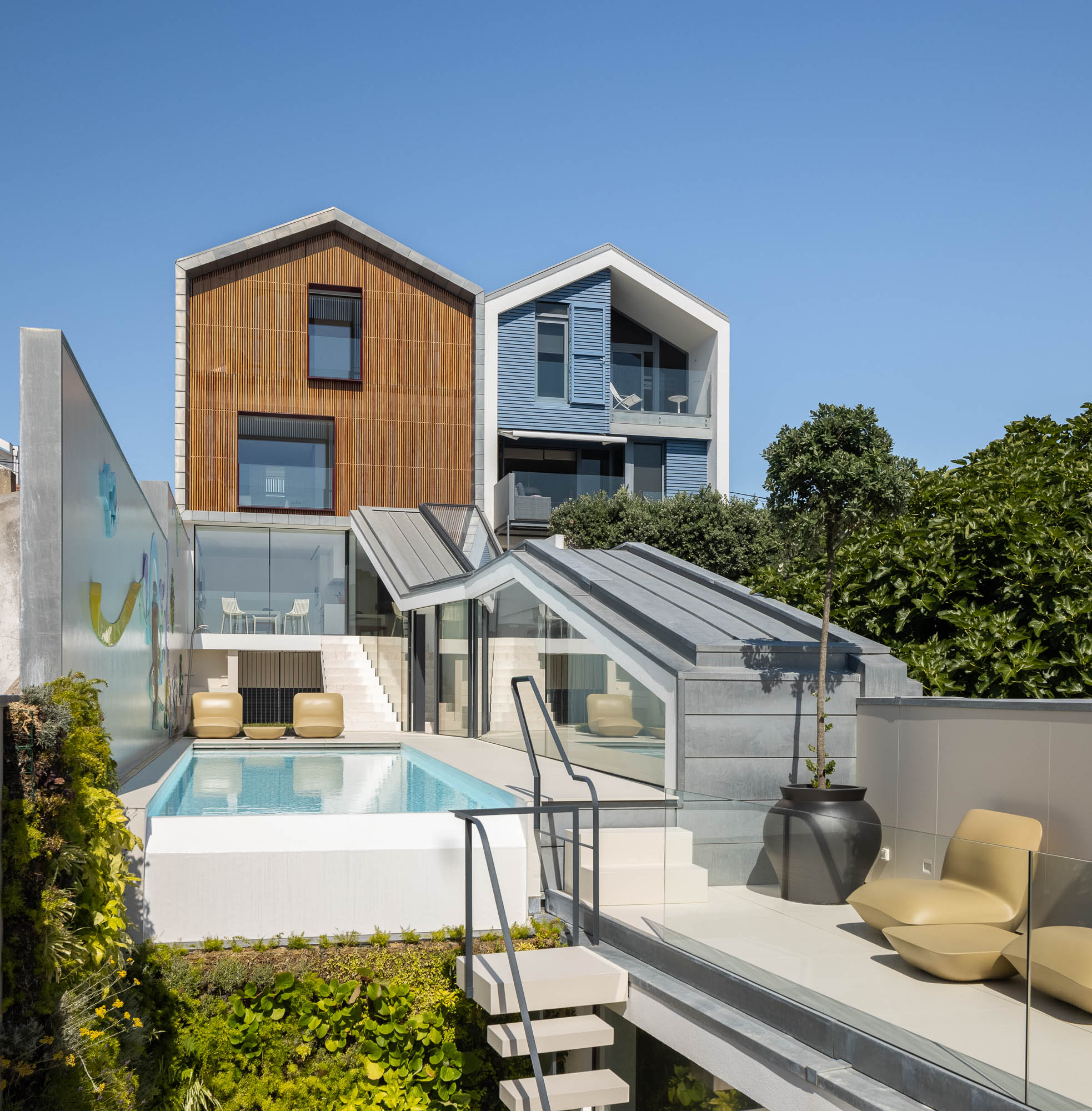 Exterior: Vista da casa com piscina, parede com mural artístico e revestimento em madeira. Integração da arquitetura na paisagem. — Casa Costa Nova arquitetura Espaço Objecto em Ílhavo