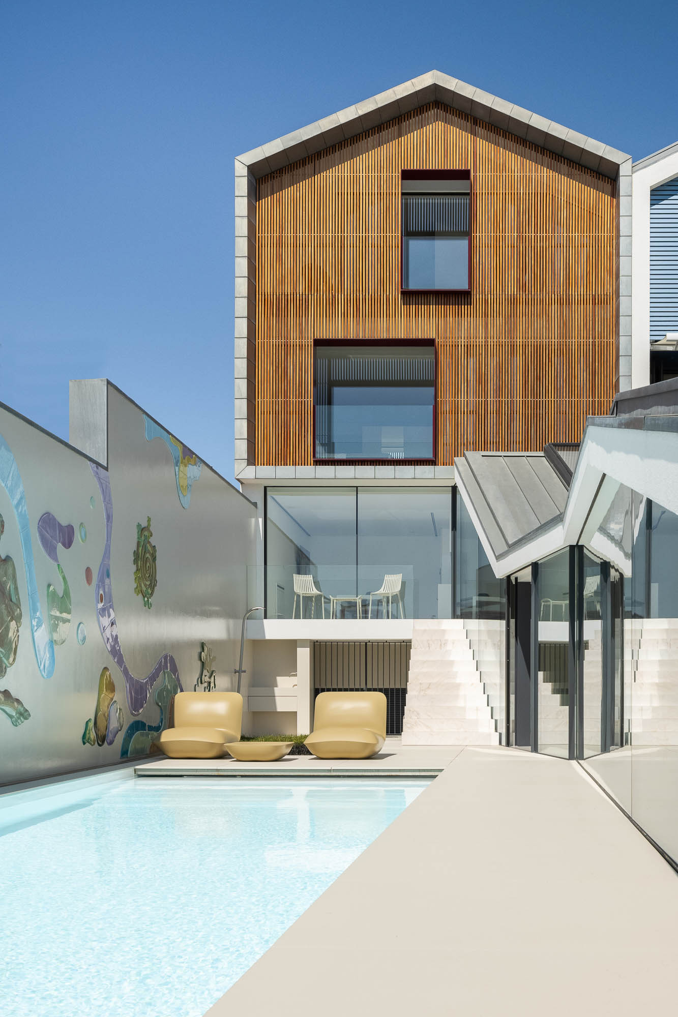 Exterior: Piscina com água azul turquesa, espreguiçadeiras e parede com painel cerâmico. Ambiente relaxante e artístico. — Casa Costa Nova arquitetura Espaço Objecto em Ílhavo