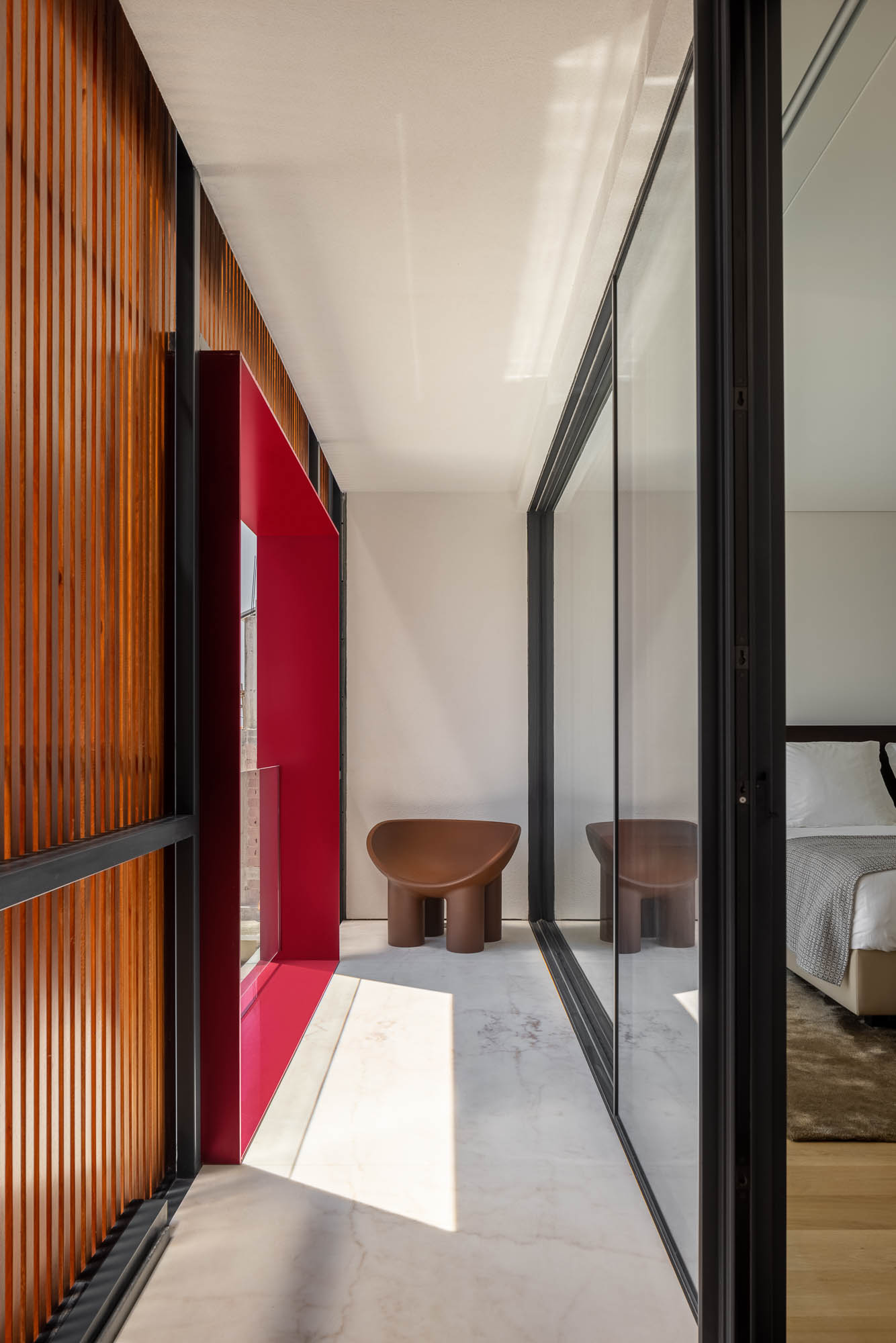 Quarto: Cama com cabeceira em madeira, banco estofado, casa de banho integrada e pavimento em madeira. Ambiente acolhedor e moderno. — Casa Costa Nova arquitetura Espaço Objecto em Ílhavo