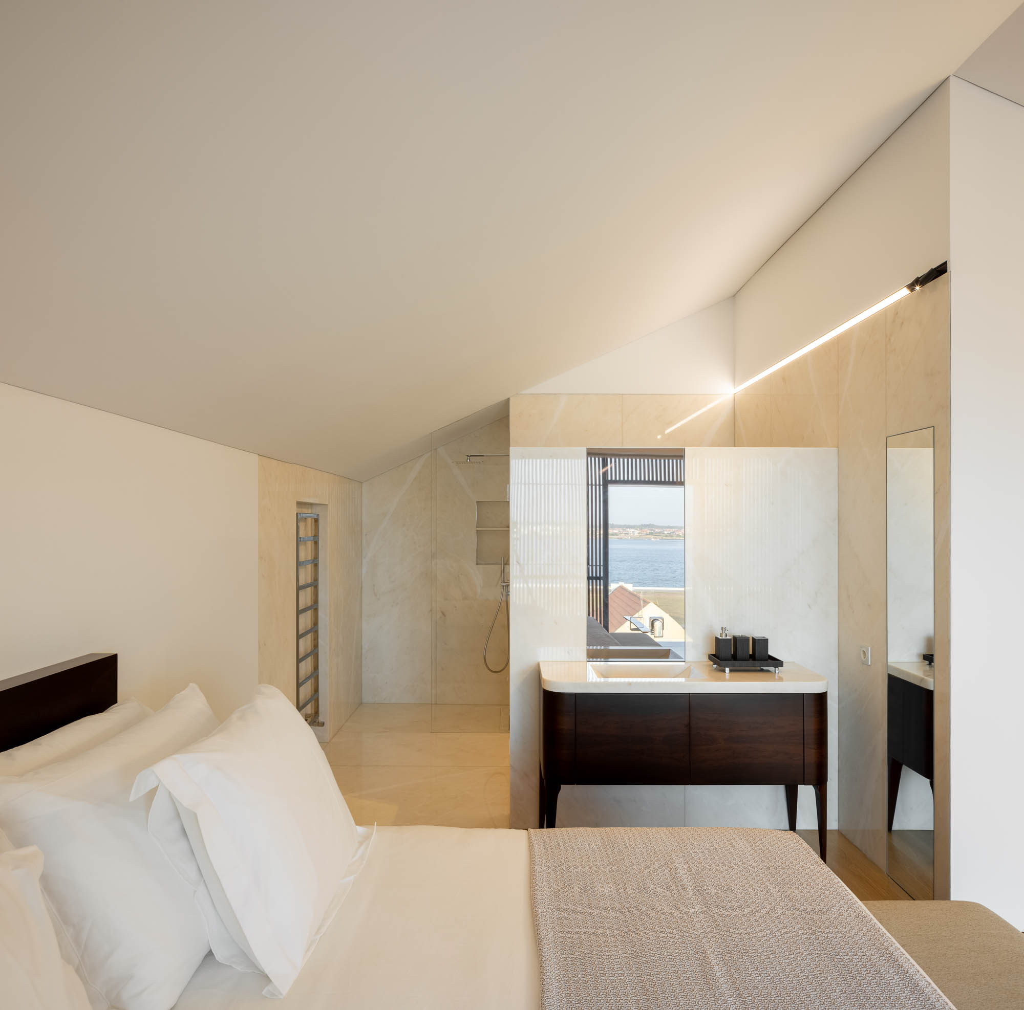 Quarto: Cama com roupa de cama laranja, casa de banho integrada com lavatório em mármore branco e pavimento em madeira. — Casa Costa Nova arquitetura Espaço Objecto em Ílhavo