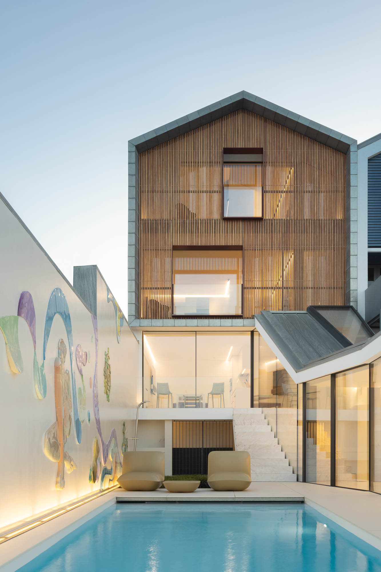 Exterior: Piscina com água azul turquesa, casa com revestimento em madeira e parede com mural artístico. Ambiente relaxante e moderno. — Casa Costa Nova arquitetura Espaço Objecto em Ílhavo