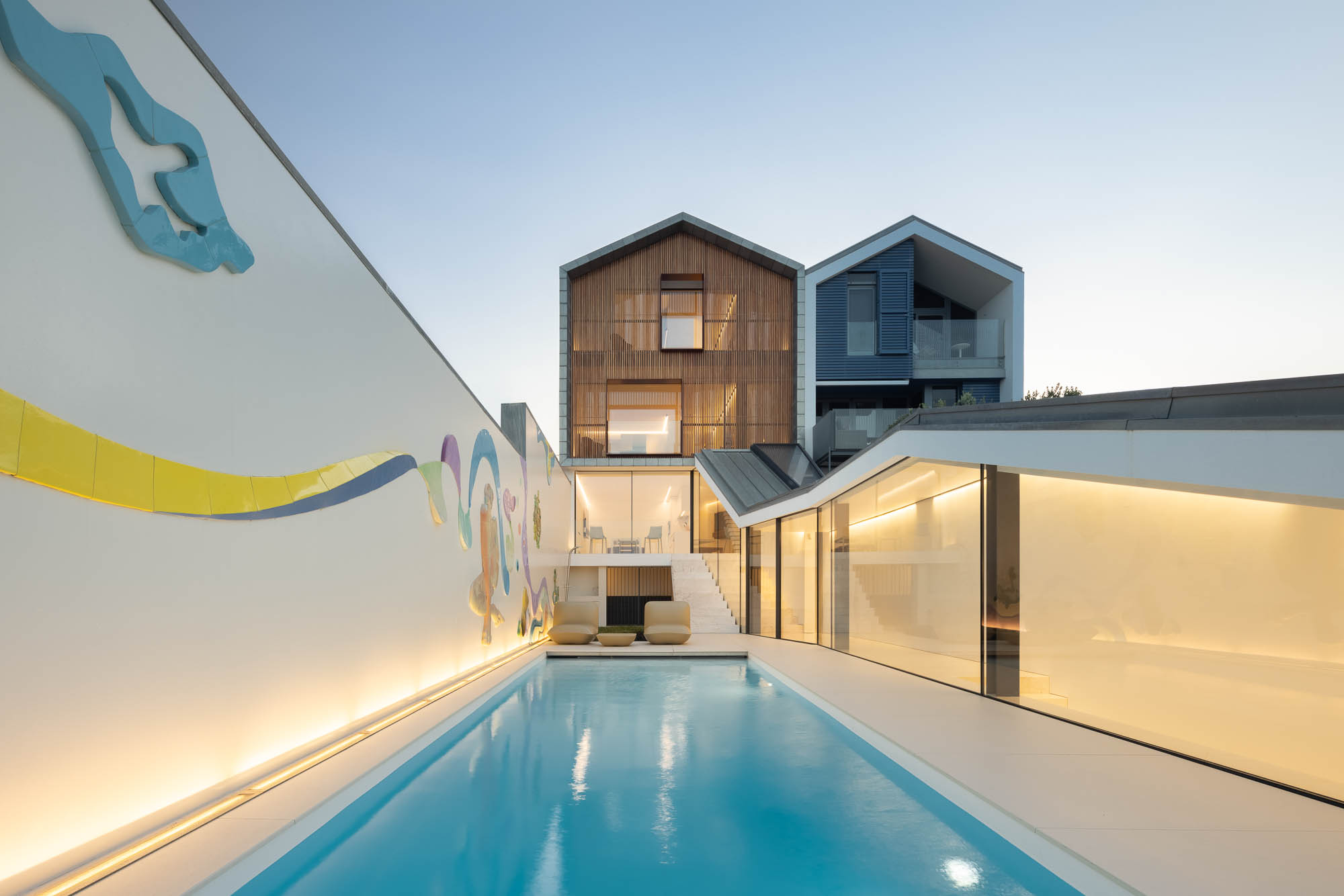 Exterior: Detalhe da casa com revestimento em madeira, janelas iluminadas e design moderno. Arquitetura contemporânea. — Casa Costa Nova arquitetura Espaço Objecto em Ílhavo
