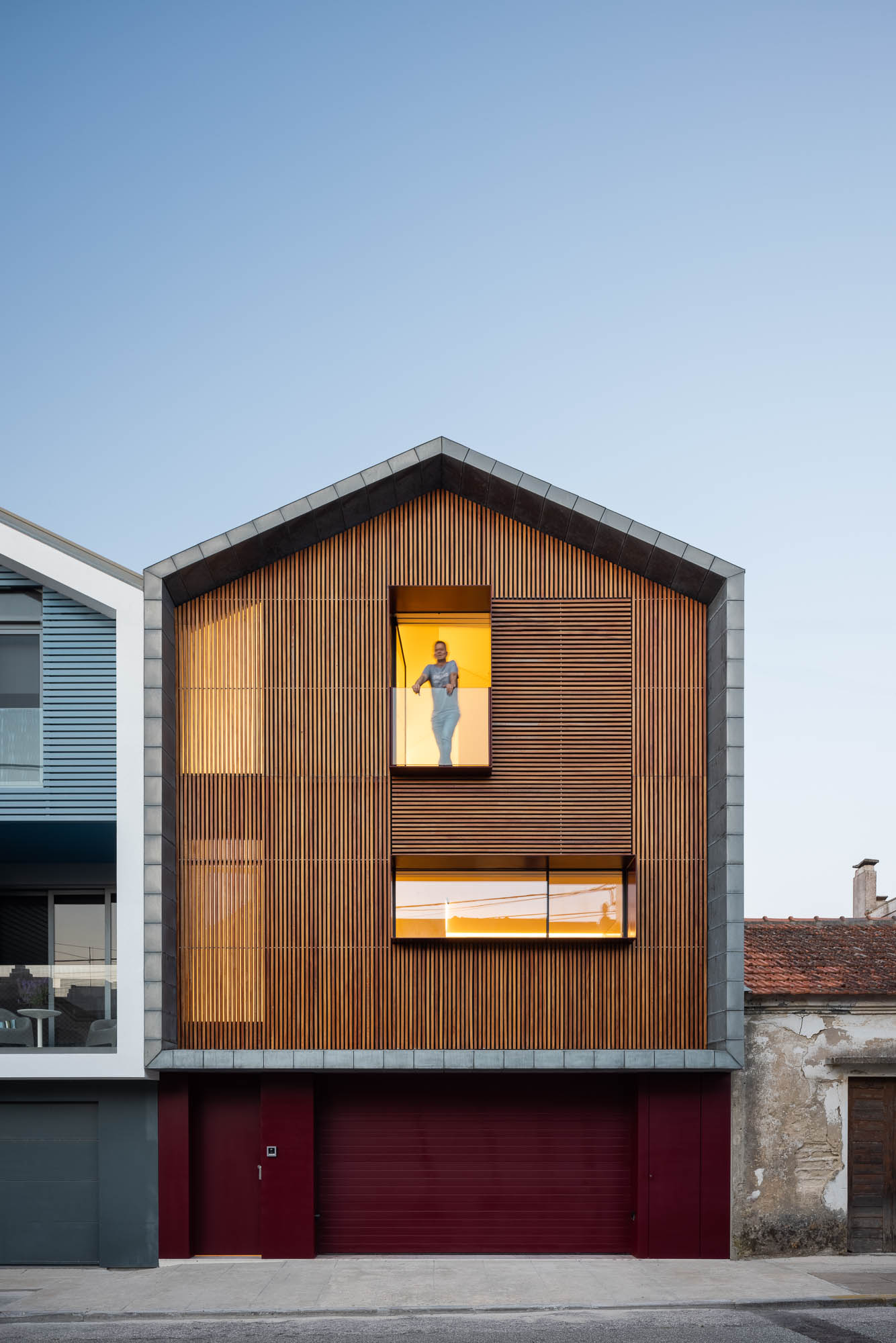 Cozinha: Vista da cozinha com mesa de jantar, pátio com lareira e casa com revestimento em madeira. Integração de espaços. — Casa Costa Nova arquitetura Espaço Objecto em Ílhavo