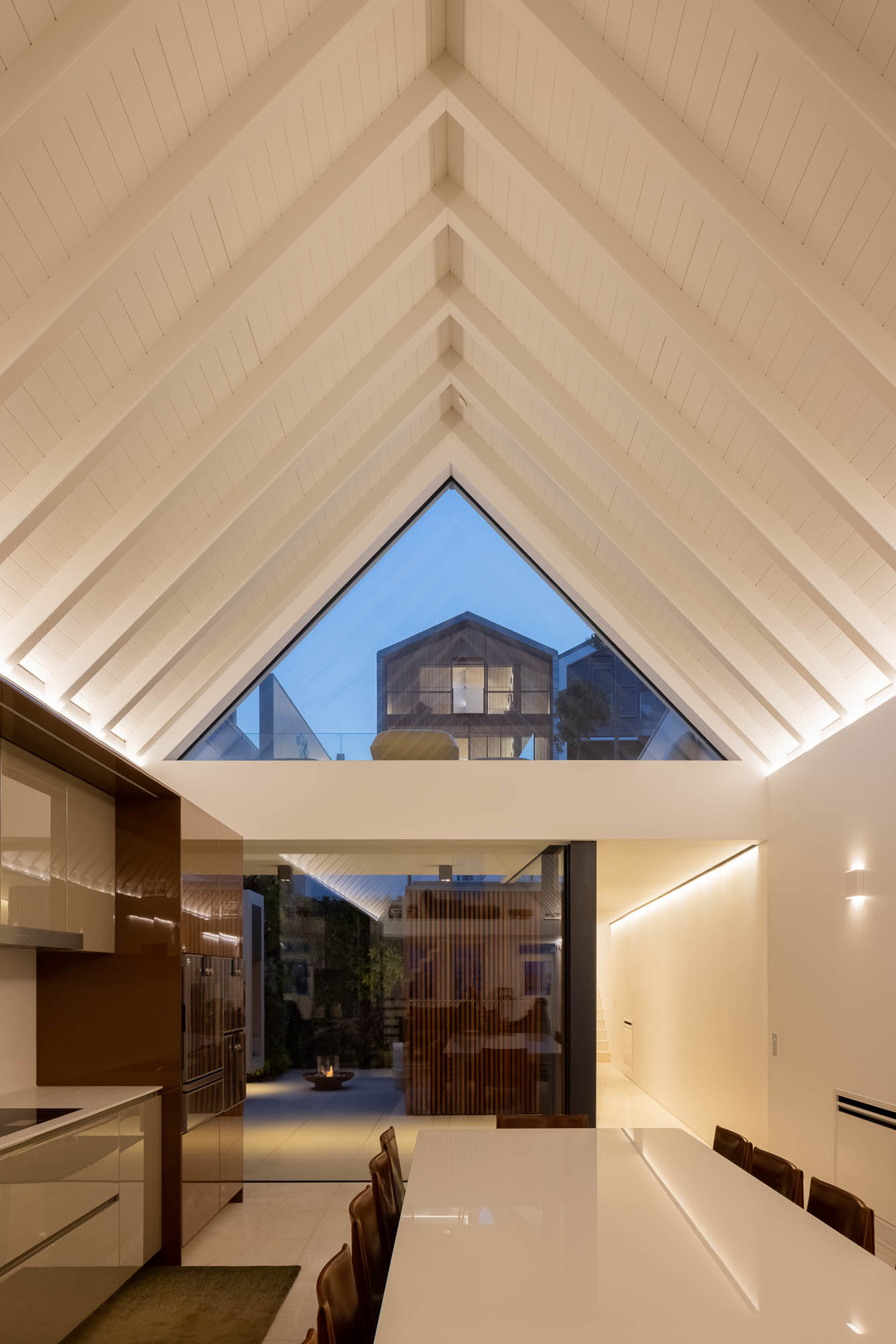 Cozinha: Vista da cozinha com mesa de jantar, pátio com lareira e casa com revestimento em madeira. Ambiente acolhedor e moderno. — Casa Costa Nova arquitetura Espaço Objecto em Ílhavo