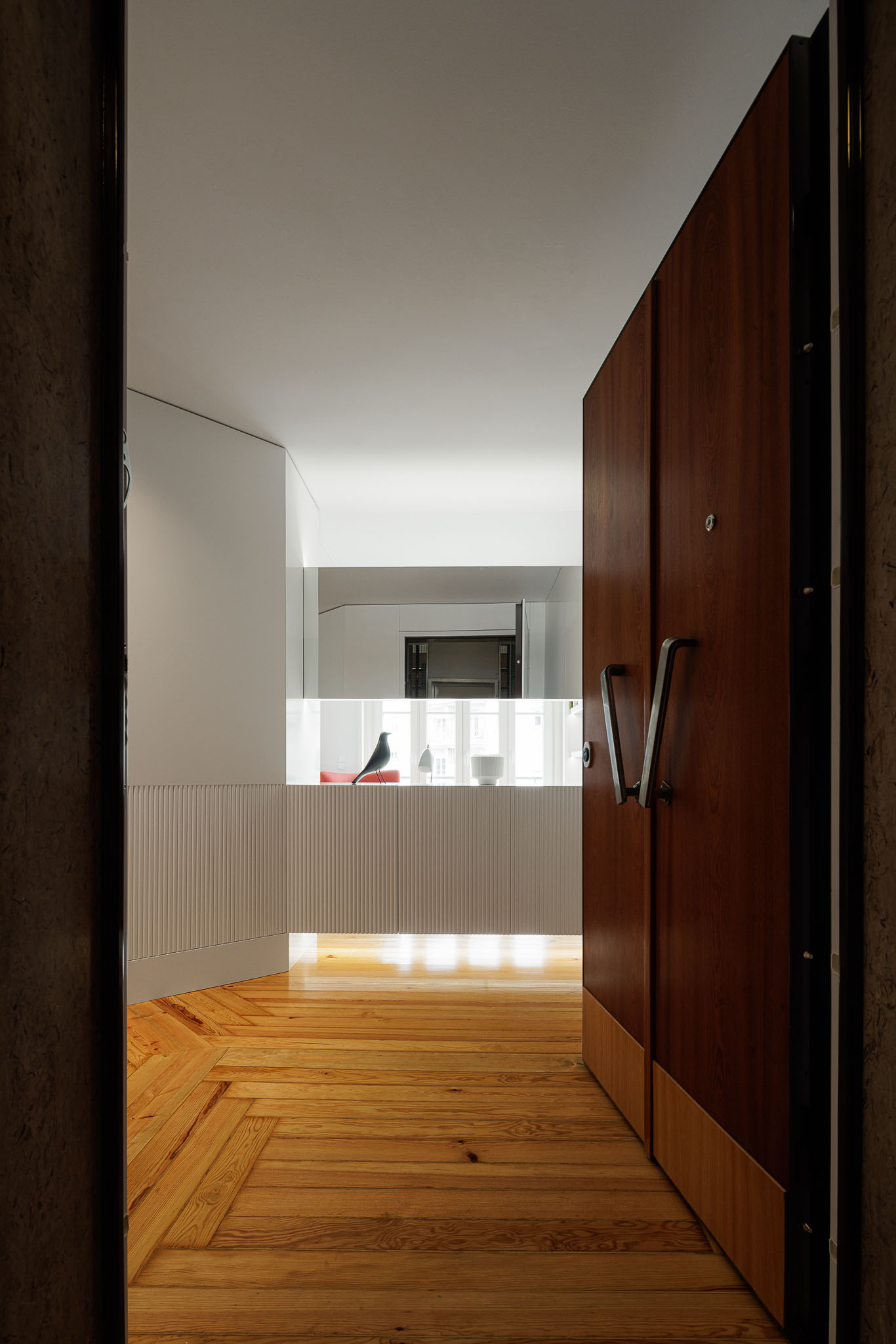 Entrada: Porta de madeira escura, pavimento em espinha de peixe e consola branca com apontamentos decorativos. — Apartamento AN arquitetura NMDARQ – Nuno Miguel Dias, Arquitecto em Lisboa