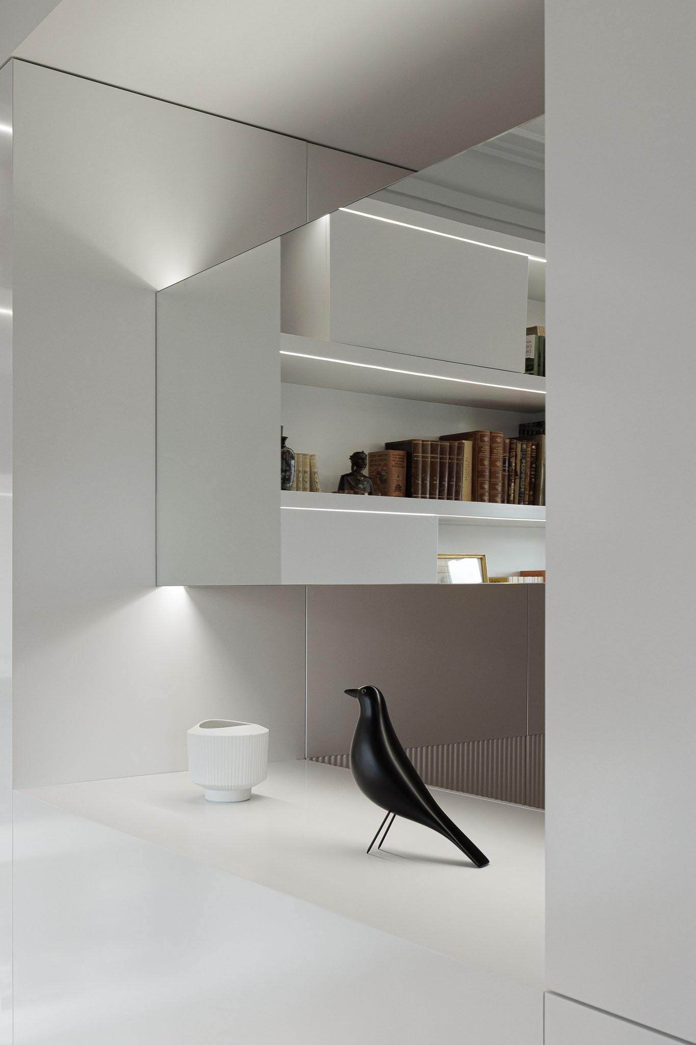 Hall de entrada: Consola branca com iluminação, elementos decorativos e espelho que reflecte a estante do escritório. — Apartamento AN arquitetura NMDARQ – Nuno Miguel Dias, Arquitecto em Lisboa