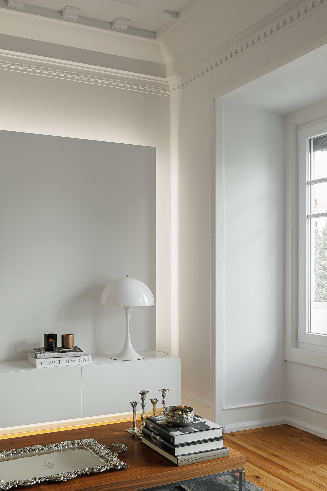 Sala de estar: Candeeiro branco de design, livros e objetos decorativos sobre aparador branco iluminado. — Apartamento AN arquitetura NMDARQ – Nuno Miguel Dias, Arquitecto em Lisboa