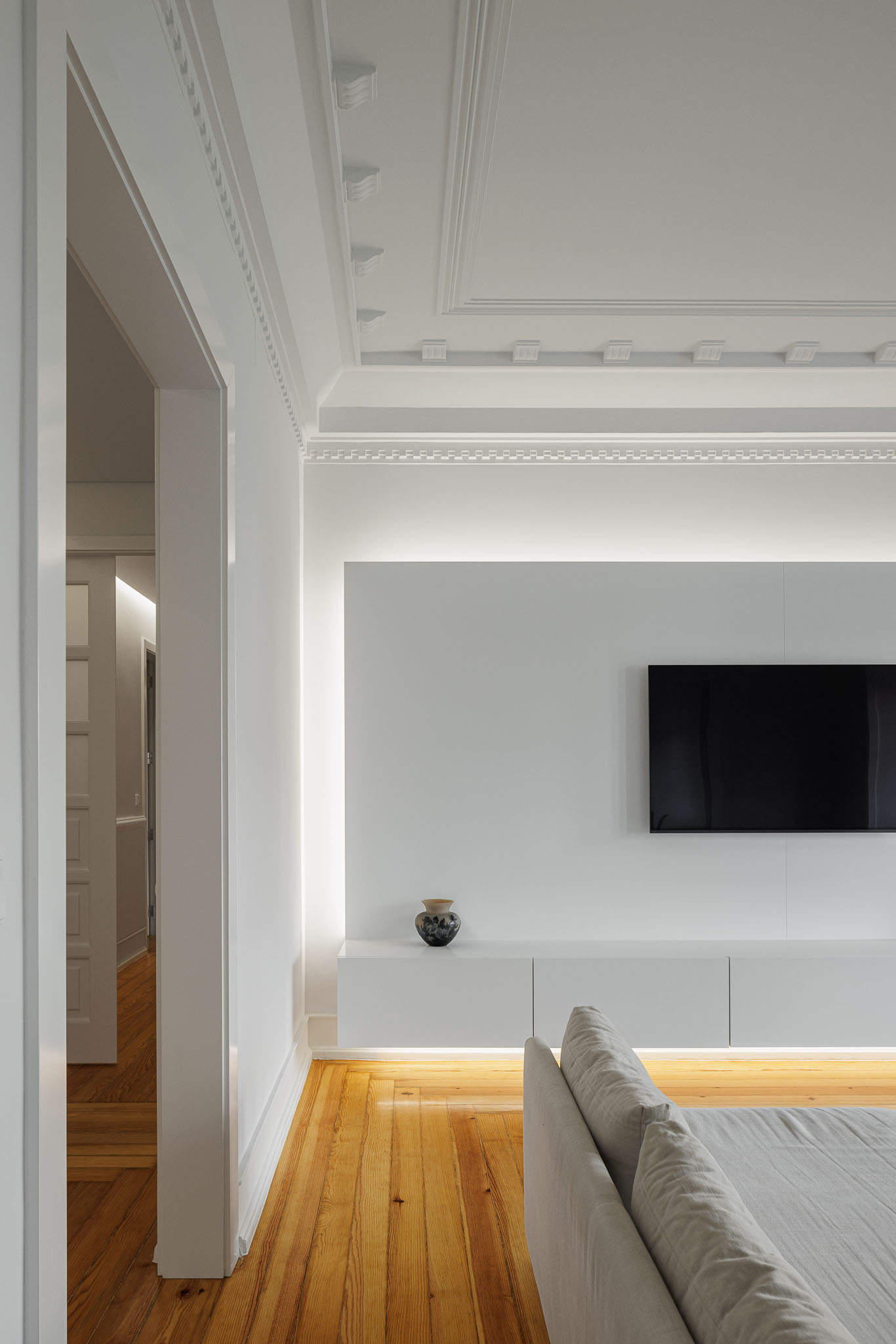 Sala de estar: Painel branco iluminado com televisão, pavimento em madeira e sofá cinzento. — Apartamento AN arquitetura NMDARQ – Nuno Miguel Dias, Arquitecto em Lisboa