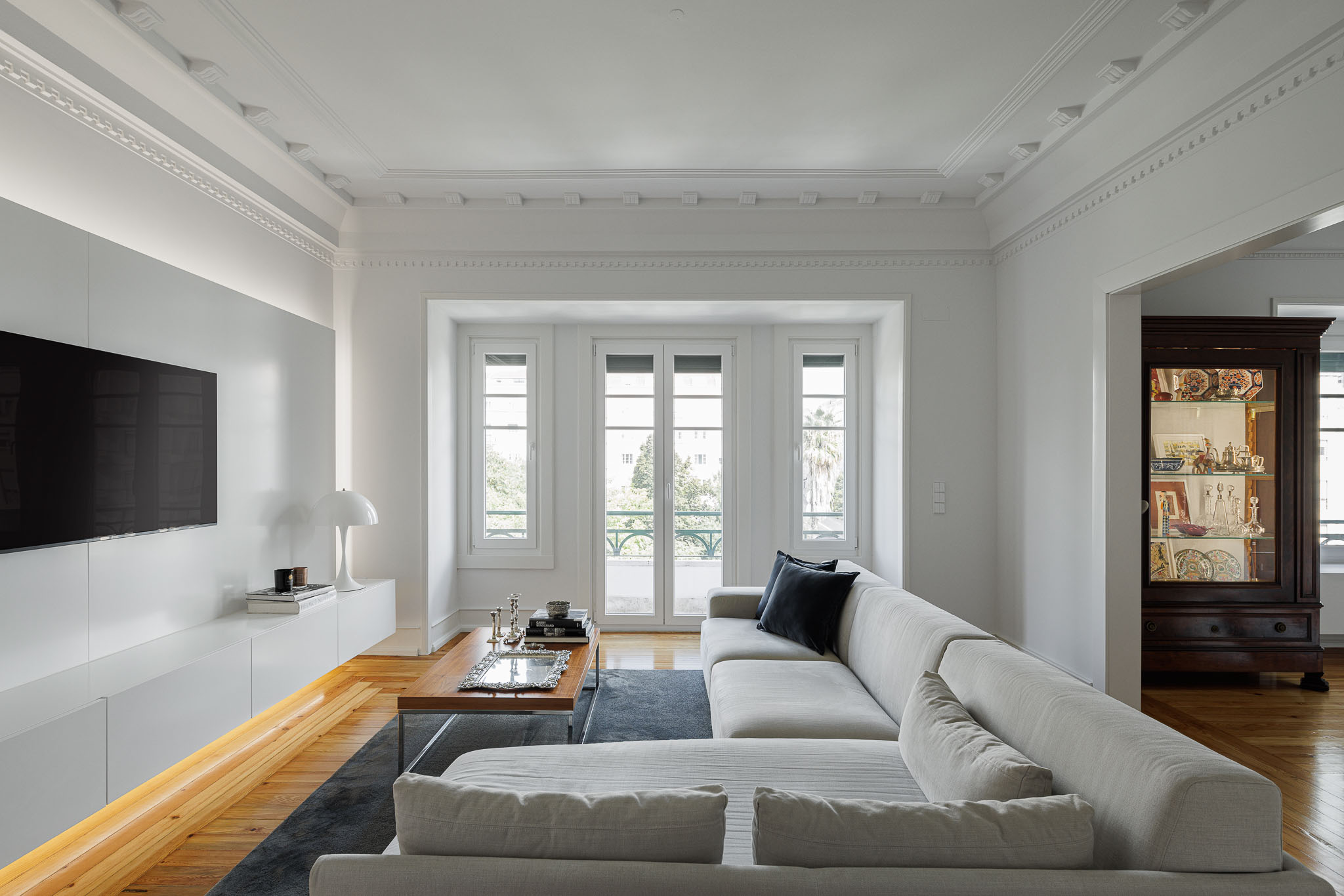 Sala de estar: Sofá cinzento, tapete escuro, painel branco com televisão e acesso à varanda com janelas brancas. — Apartamento AN arquitetura NMDARQ – Nuno Miguel Dias, Arquitecto em Lisboa