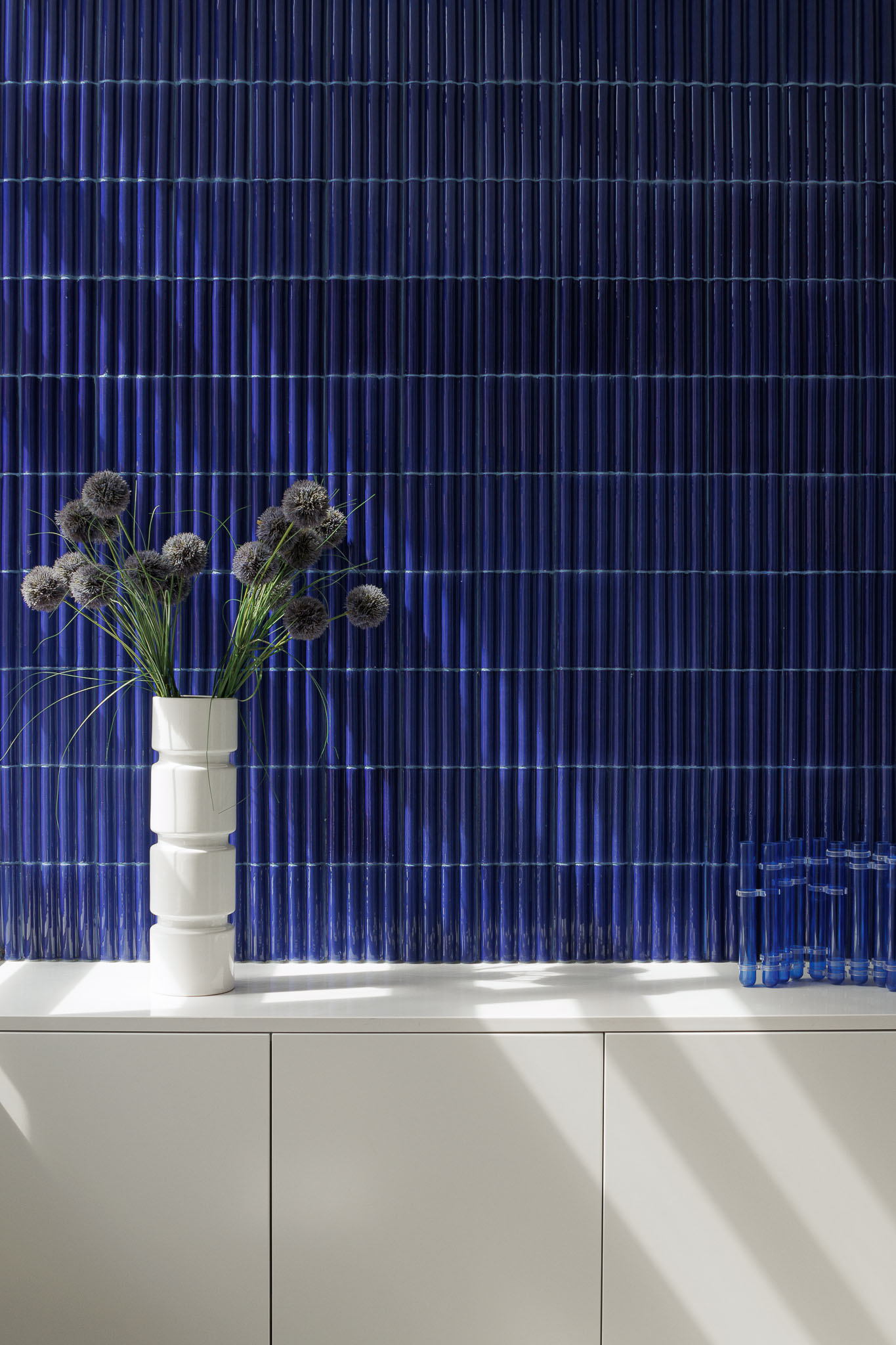 Cozinha: Azulejo azul vertical, armários brancos e vaso branco com arranjo floral. — Apartamento AN arquitetura NMDARQ – Nuno Miguel Dias, Arquitecto em Lisboa