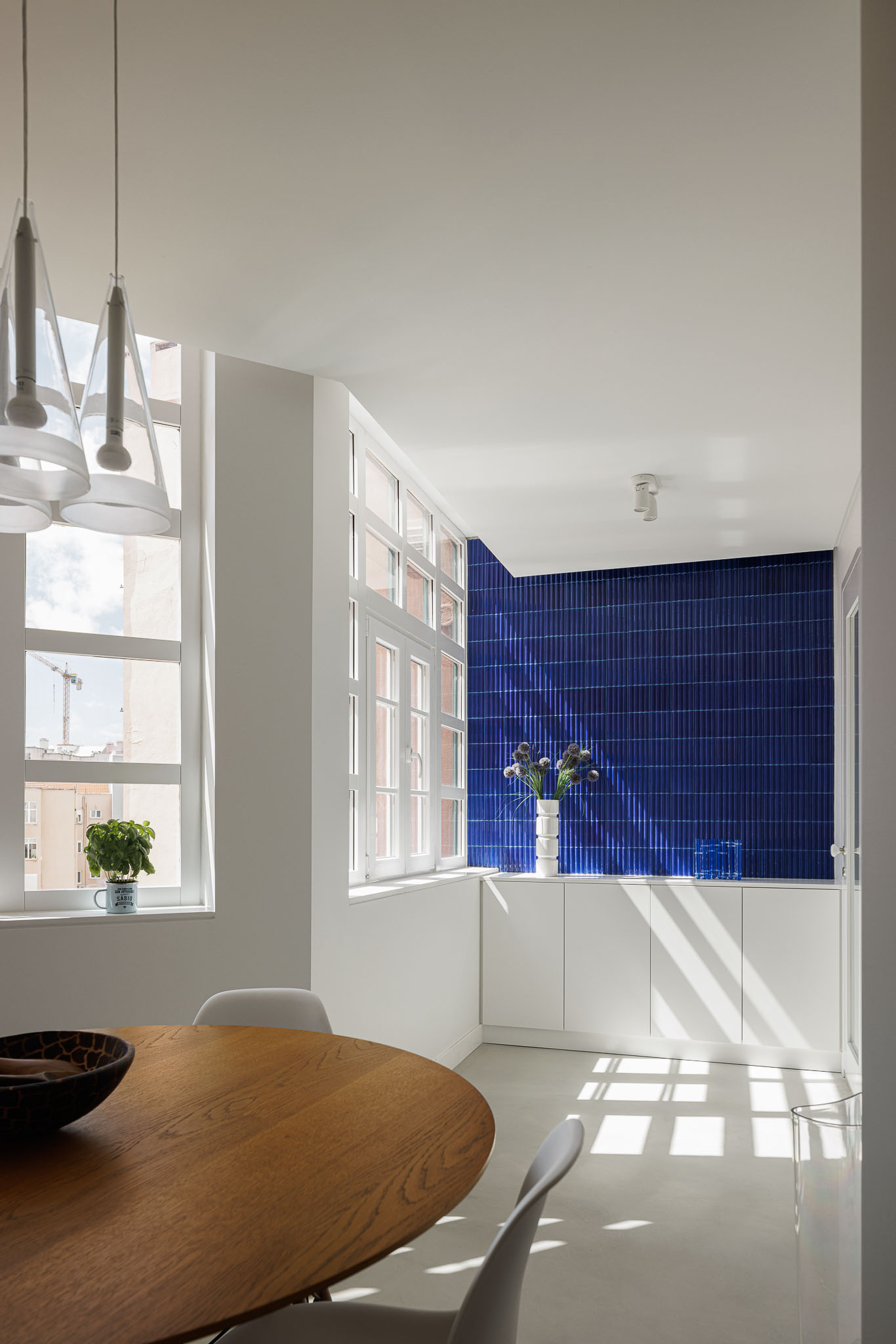 Cozinha: Mesa de madeira redonda, cadeiras brancas e vista para o backsplash azul. — Apartamento AN arquitetura NMDARQ – Nuno Miguel Dias, Arquitecto em Lisboa