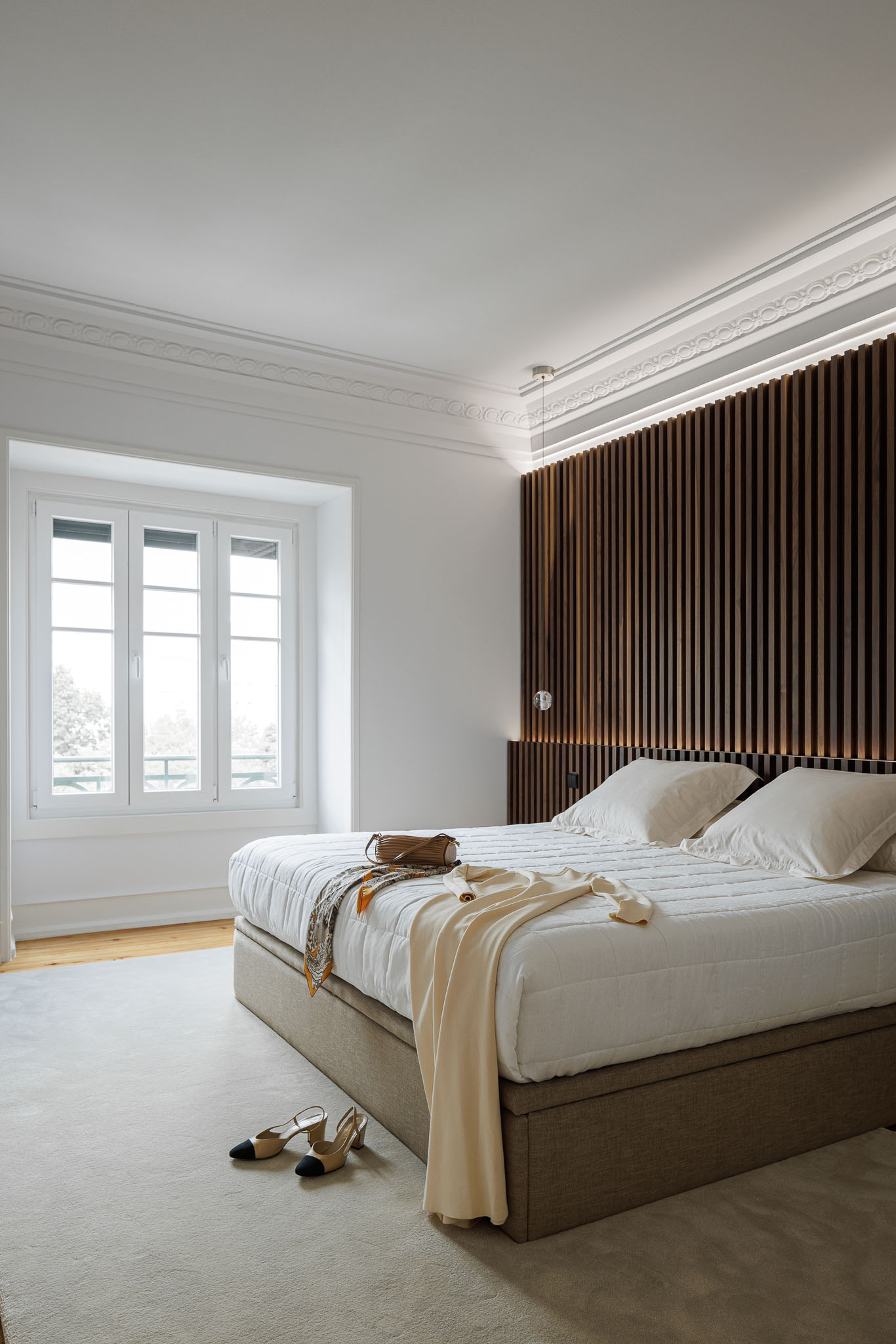 Quarto: Cama com cabeceira em ripas de madeira escura, candeeiro suspenso e alcatifa clara. — Apartamento AN arquitetura NMDARQ – Nuno Miguel Dias, Arquitecto em Lisboa