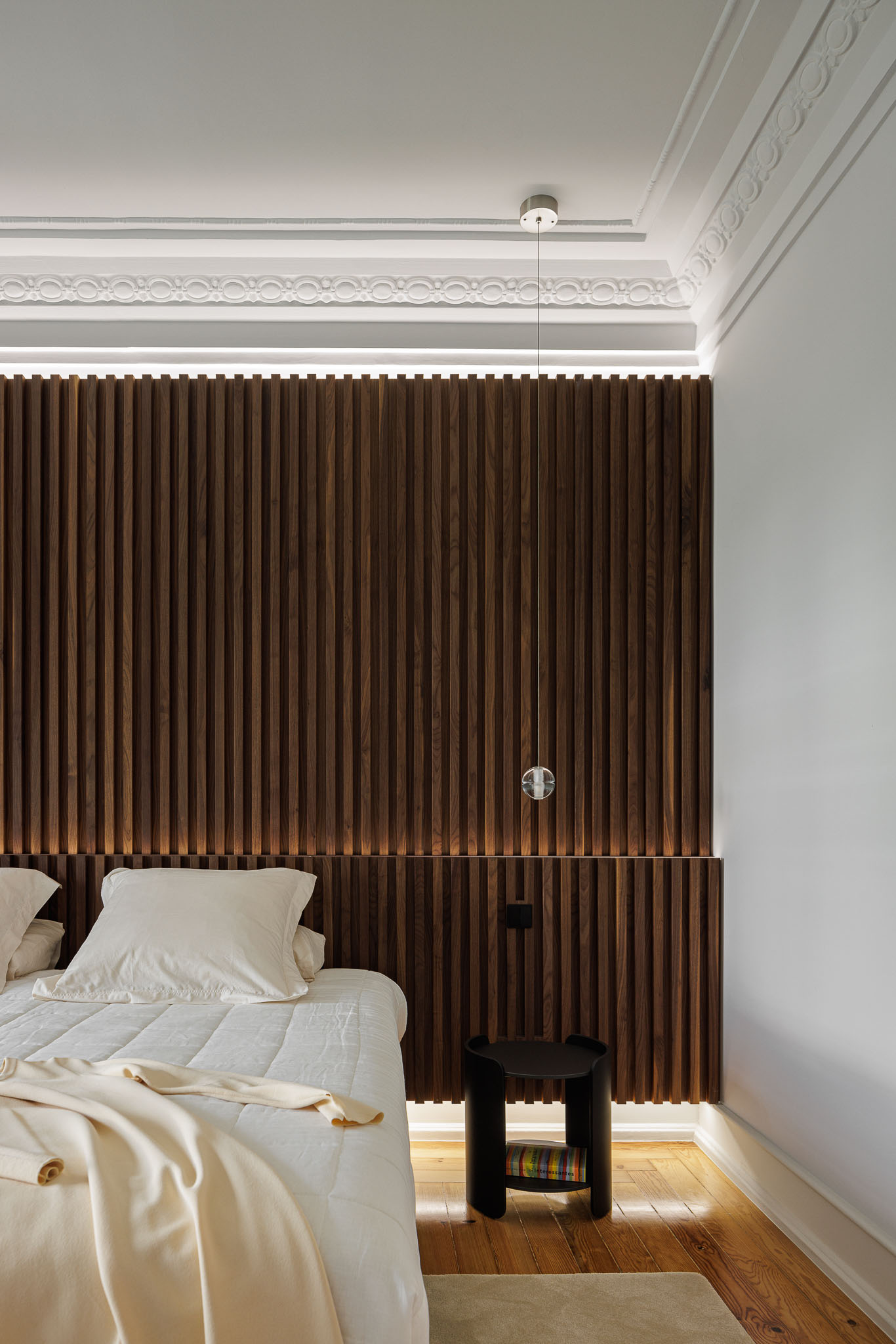Quarto: Cabeceira em ripas de madeira escura com iluminação, mesa de cabeceira preta e pavimento em madeira. — Apartamento AN arquitetura NMDARQ – Nuno Miguel Dias, Arquitecto em Lisboa