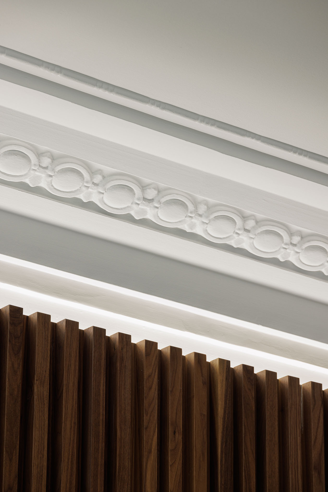 Quarto: Detalhe da cabeceira em ripas de madeira escura com iluminação e moldura clássica no teto. — Apartamento AN arquitetura NMDARQ – Nuno Miguel Dias, Arquitecto em Lisboa