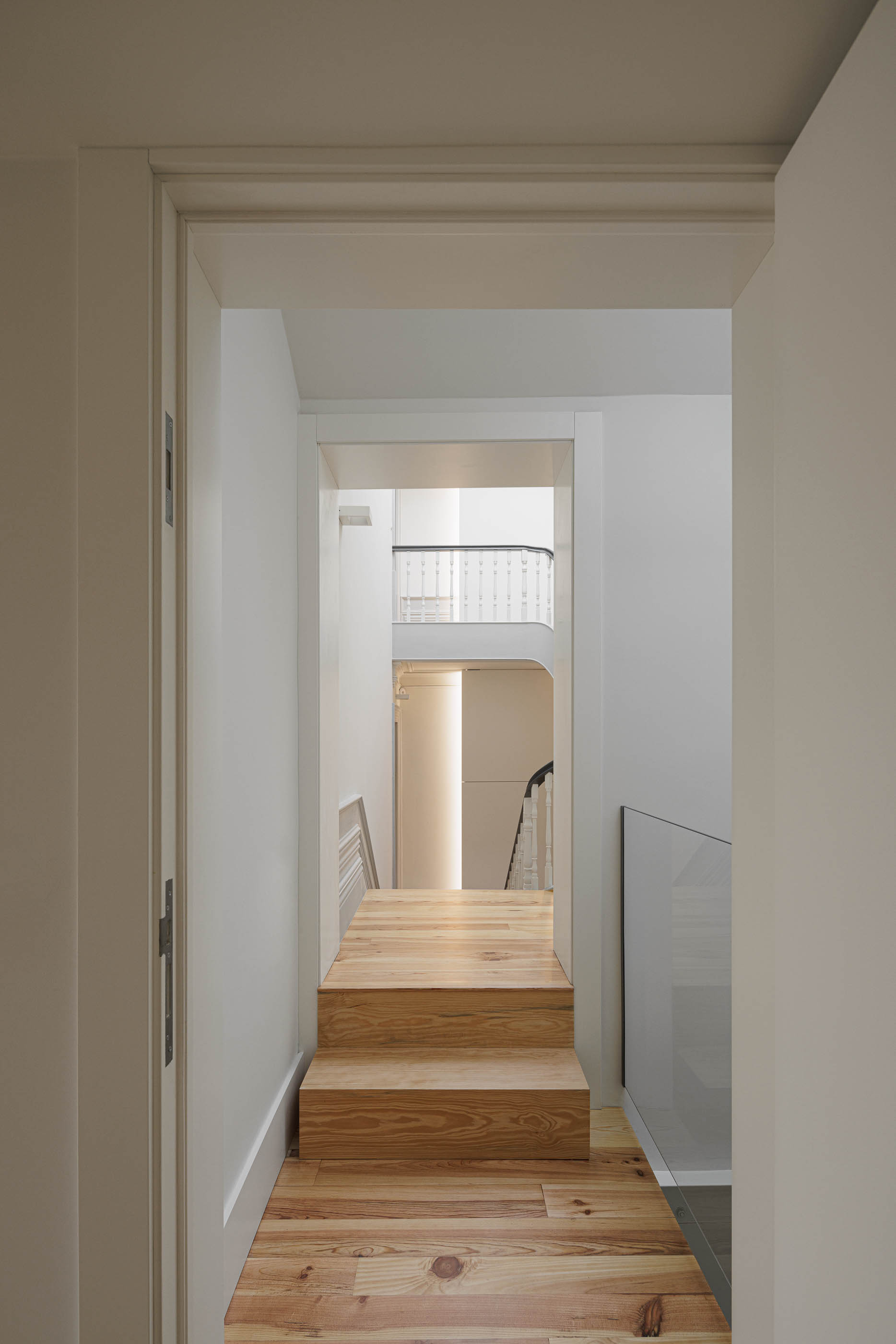 Corredor: Escadas em madeira clara, corrimão preto e porta branca. — Marlim D. João IV arquitetura Atelier d´Arquitectura Lopes da Costa em Porto