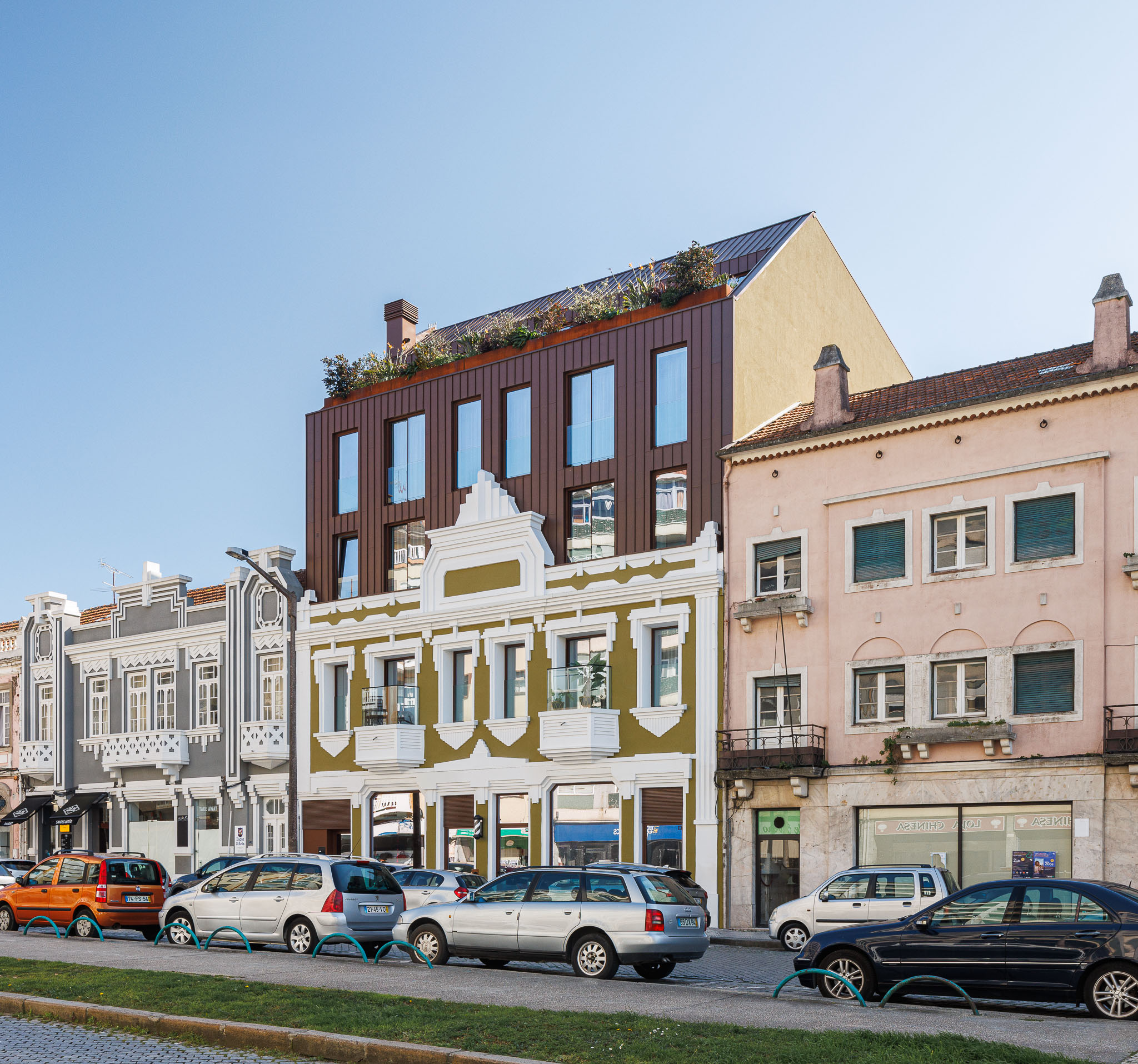 Fachada: Edifício histórico renovado com adição moderna em cobre e cobertura ajardinada, integrado na rua. — 5ª Avenida arquitetura Mário Alves Arquitecto em Aveiro