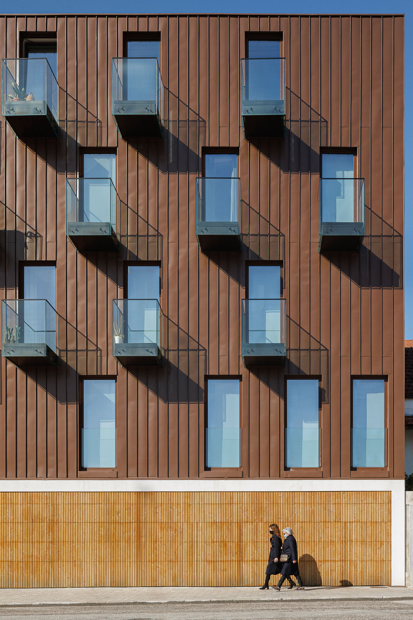 Fachada: Detalhe da fachada moderna em cobre com varandas de vidro e base em madeira ripada. — 5ª Avenida arquitetura Mário Alves Arquitecto em Aveiro
