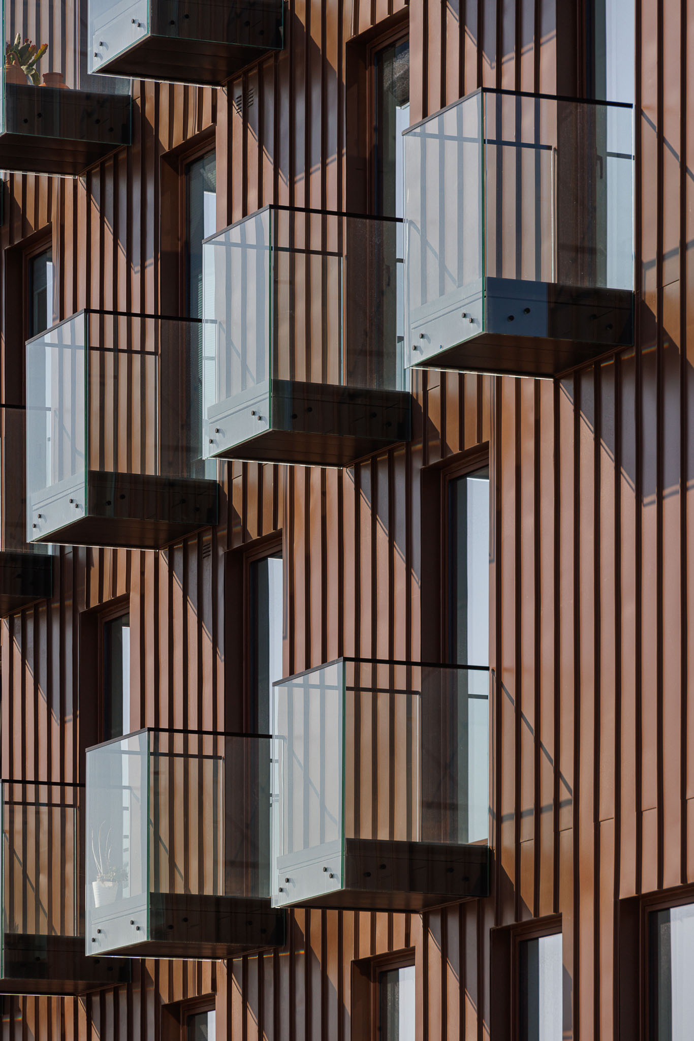 Fachada: Close-up das varandas de vidro da fachada em cobre, com plantas. — 5ª Avenida arquitetura Mário Alves Arquitecto em Aveiro