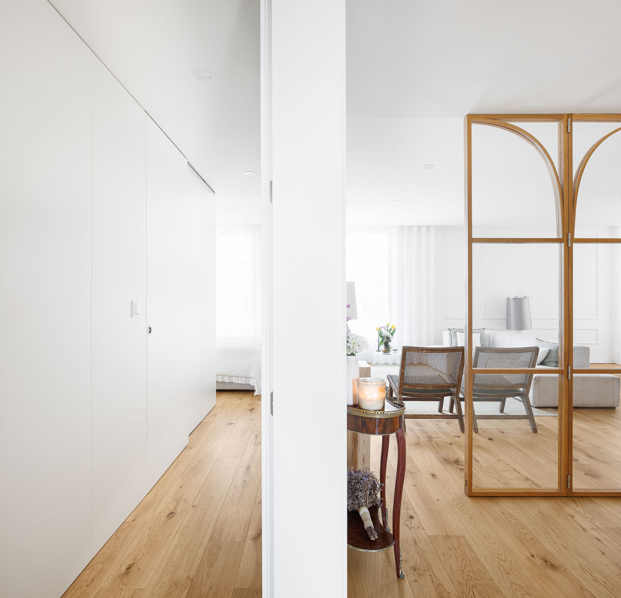 Corredor: Vista do corredor para a sala de estar através da divisória em vidro e madeira, com armários brancos. — 5ª Avenida arquitetura Mário Alves Arquitecto em Aveiro