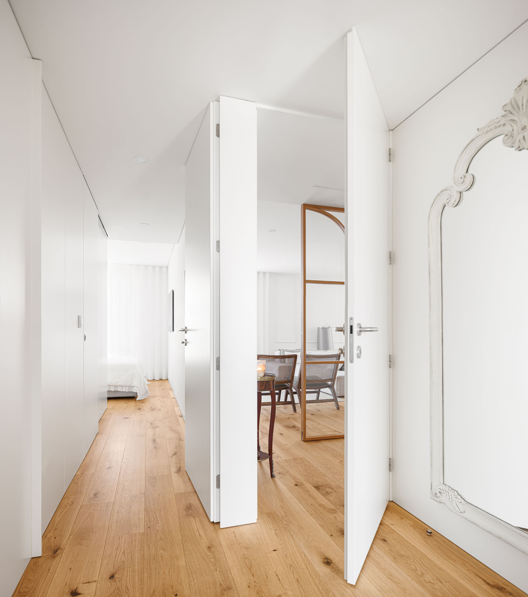 Corredor: Porta aberta revela o corredor com armários brancos, pavimento em madeira e vista para a sala. — 5ª Avenida arquitetura Mário Alves Arquitecto em Aveiro
