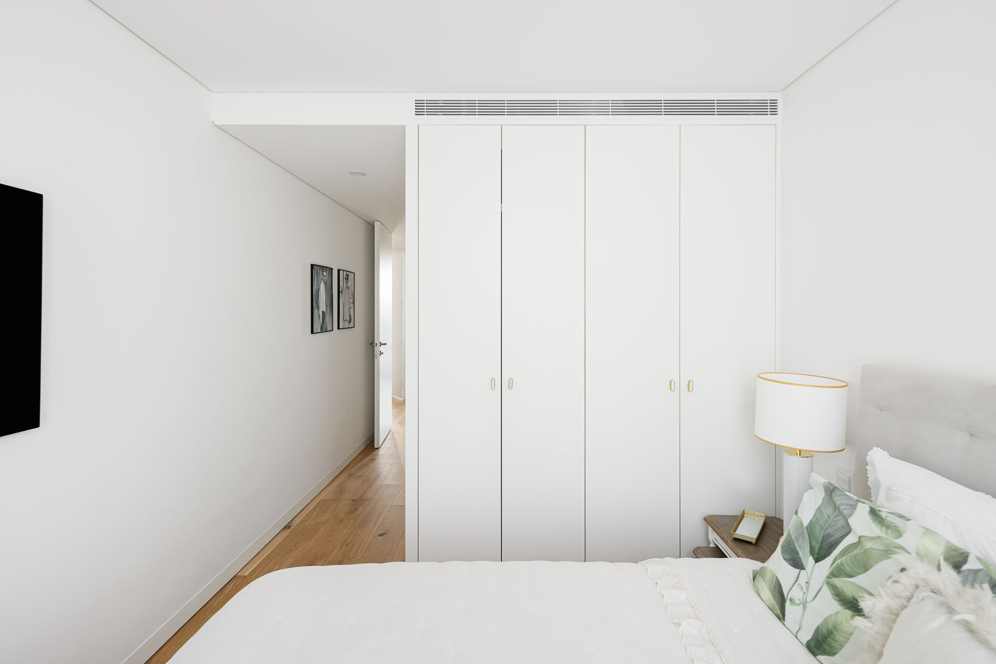 Quarto: Cama com cabeceira cinza, armários brancos embutidos e vista para o corredor. — 5ª Avenida arquitetura Mário Alves Arquitecto em Aveiro