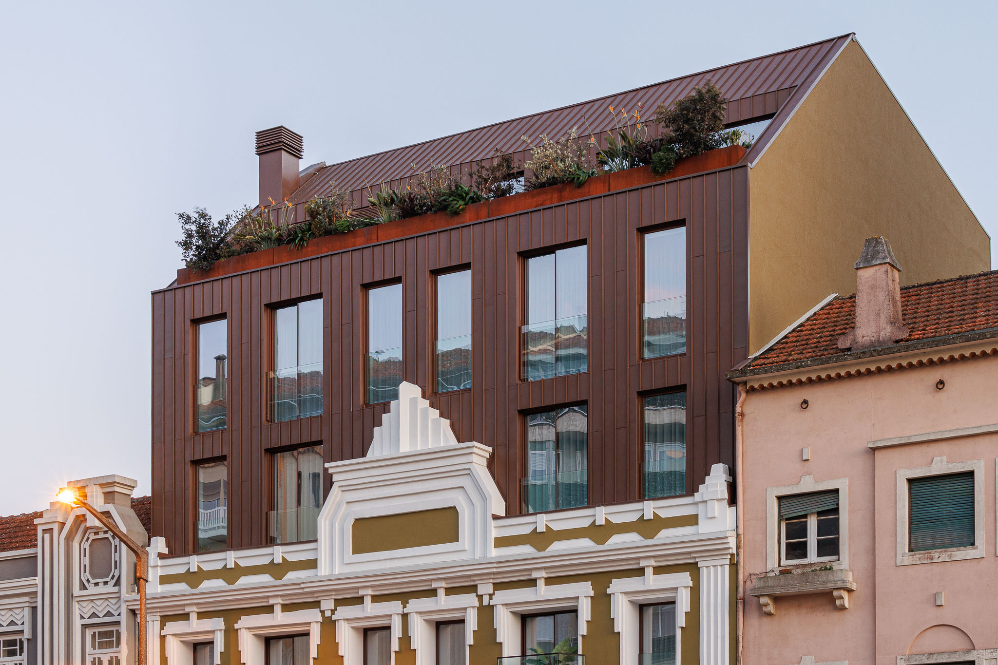 Fachada: Vista superior do edifício renovado, destacando a fachada em cobre e a cobertura ajardinada. — 5ª Avenida arquitetura Mário Alves Arquitecto em Aveiro