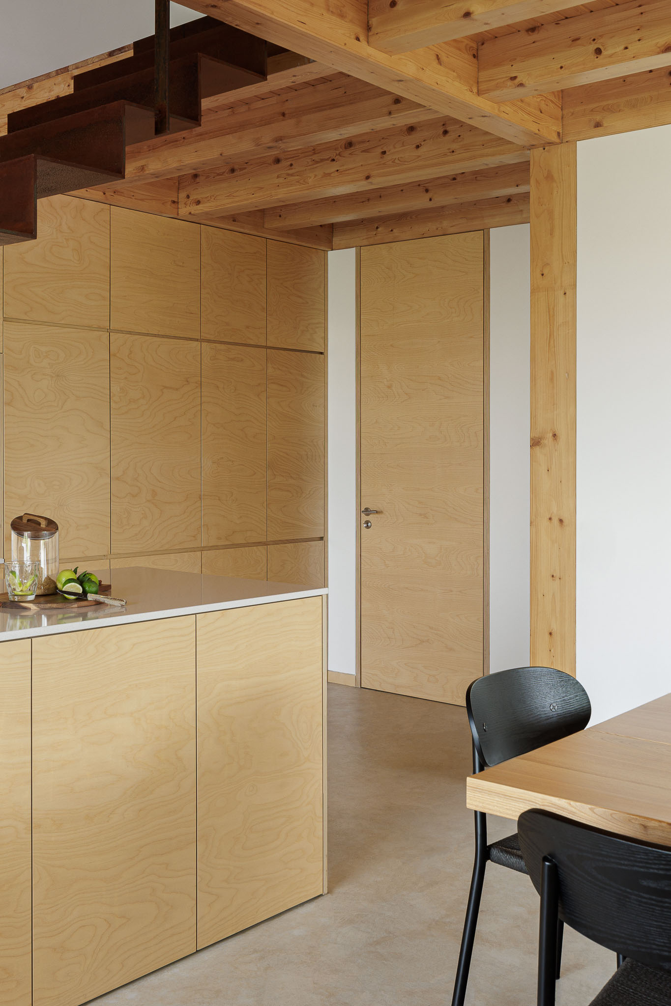 Cozinha/Sala de jantar: Ilha da cozinha em madeira clara com escada em metal oxidado. Teto em madeira e cadeiras pretas. — Palheiro arquitetura Pedro Henrique Arquiteto em Esmoriz