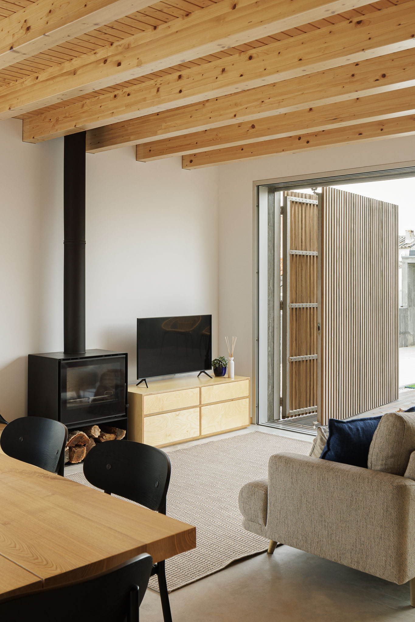 Sala de estar: Lareira preta com lenha, móvel em madeira clara e televisão. Teto em madeira. — Palheiro arquitetura Pedro Henrique Arquiteto em Esmoriz