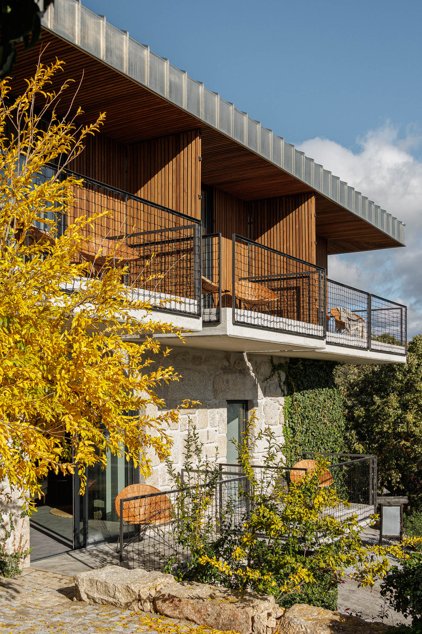 Varanda: Cadeiras de vime e mesa preta, com vista panorâmica. Guarda em rede metálica preta. — The Vagar – Country House arquitetura David Bilo Arquitectos e Filipe Pina Arquitectura em Belmonte
