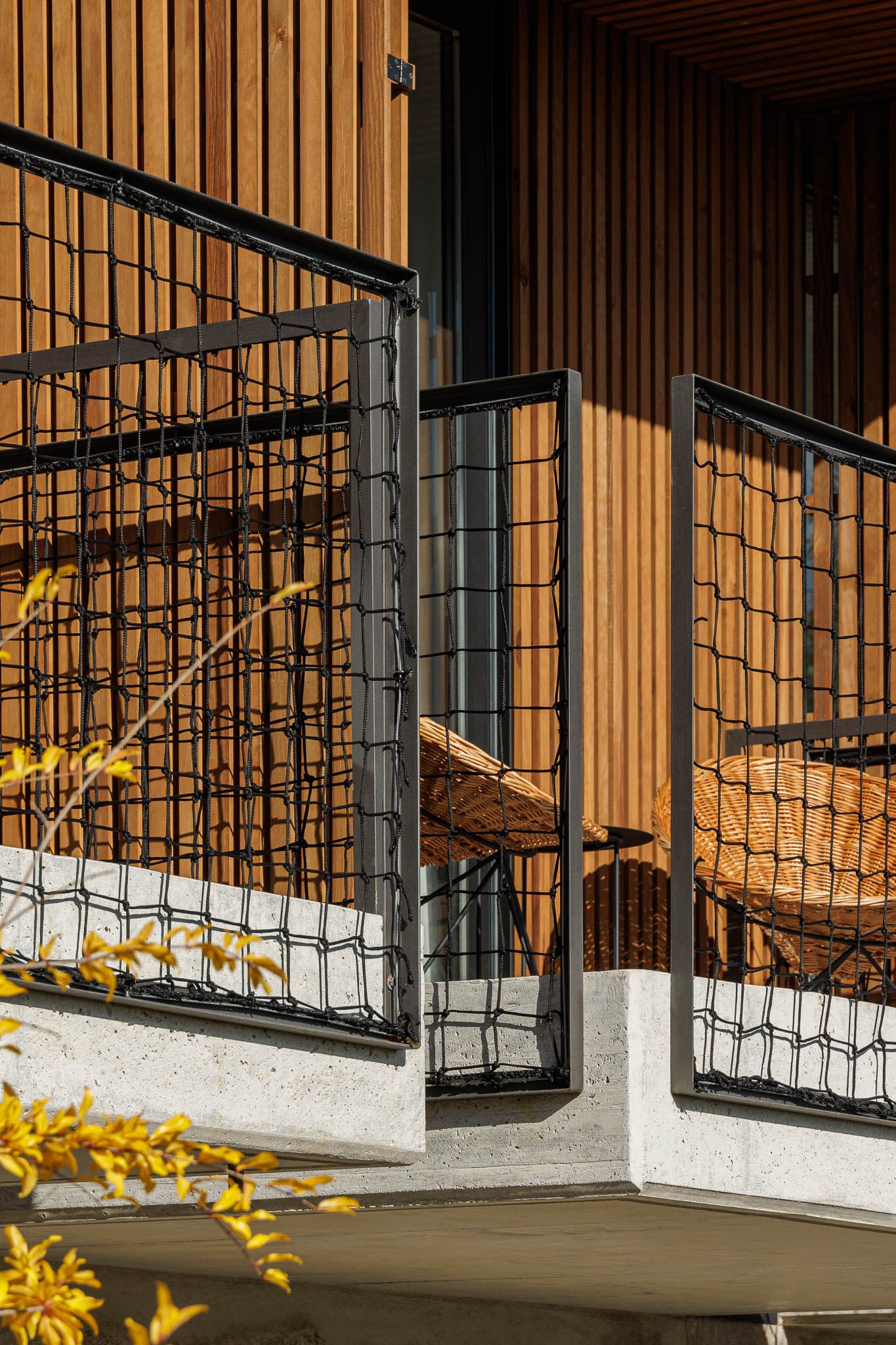 Varanda: Detalhe da guarda em rede metálica preta e cadeiras de vime. Revestimento em madeira vertical. — The Vagar – Country House arquitetura David Bilo Arquitectos e Filipe Pina Arquitectura em Belmonte