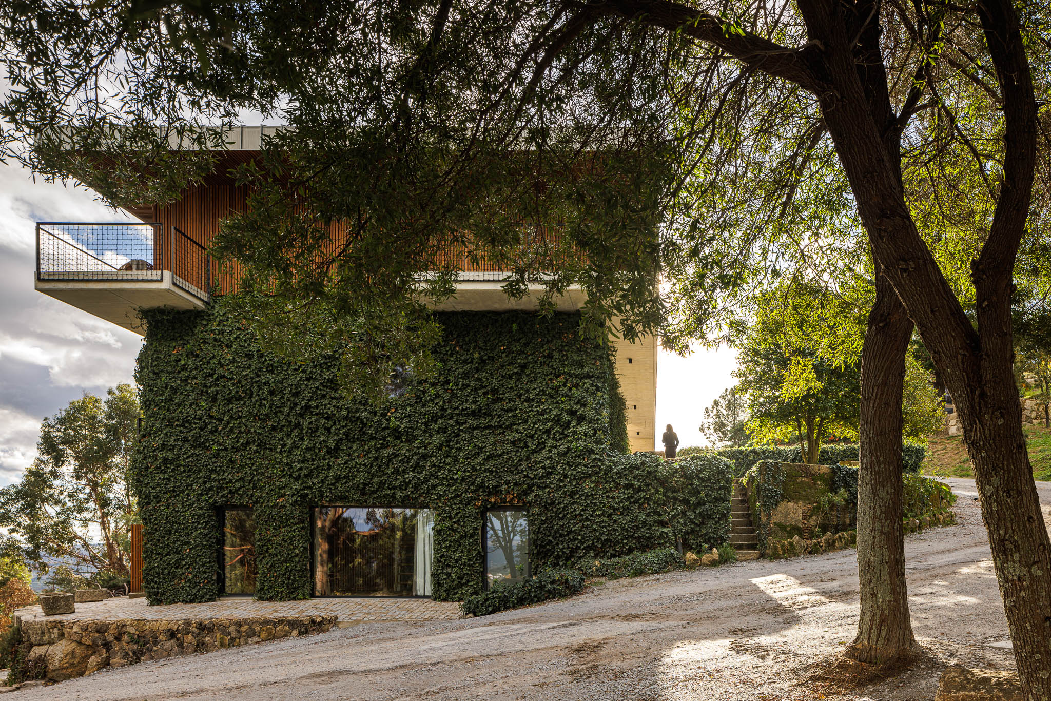 Exterior: Vista da casa de campo com fachada coberta de trepadeira, janelas e escadas de acesso. — The Vagar – Country House arquitetura David Bilo Arquitectos e Filipe Pina Arquitectura em Belmonte