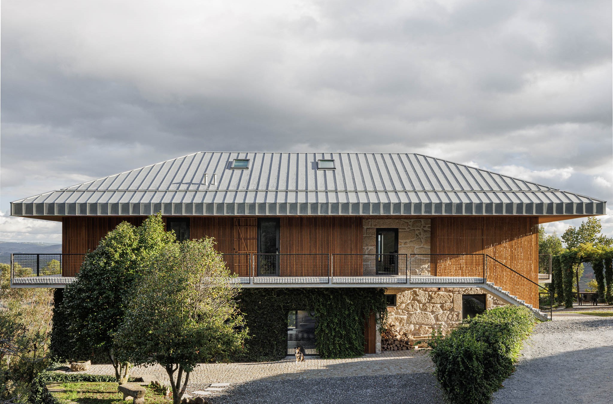 Exterior: Vista frontal da casa de campo com telhado metálico, revestimento em madeira e pedra. — The Vagar – Country House arquitetura David Bilo Arquitectos e Filipe Pina Arquitectura em Belmonte