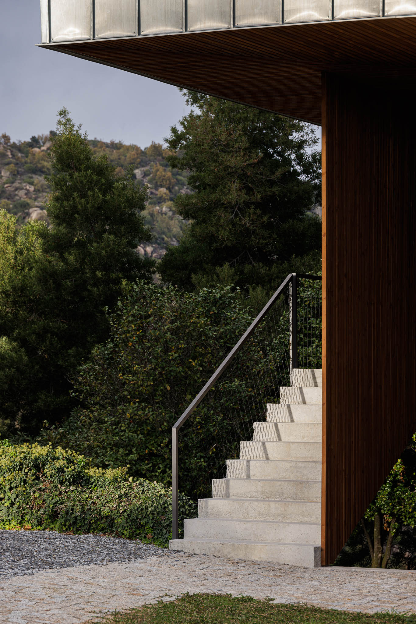 Exterior: Escadas de acesso em betão com guarda em rede metálica preta. Revestimento em madeira vertical. — The Vagar – Country House arquitetura David Bilo Arquitectos e Filipe Pina Arquitectura em Belmonte