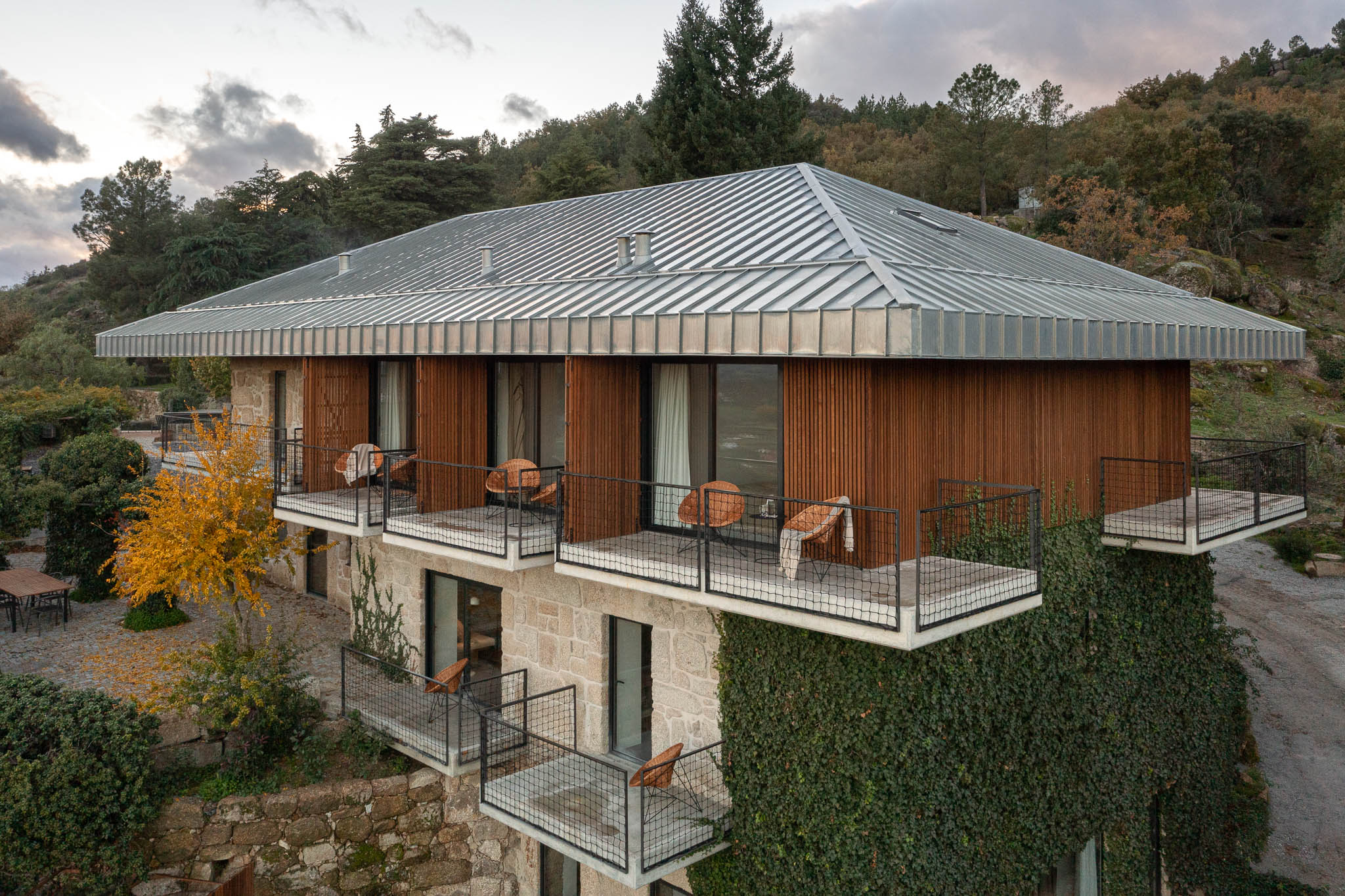 Exterior: Vista da casa de campo com varandas e revestimento em pedra e madeira. — The Vagar – Country House arquitetura David Bilo Arquitectos e Filipe Pina Arquitectura em Belmonte