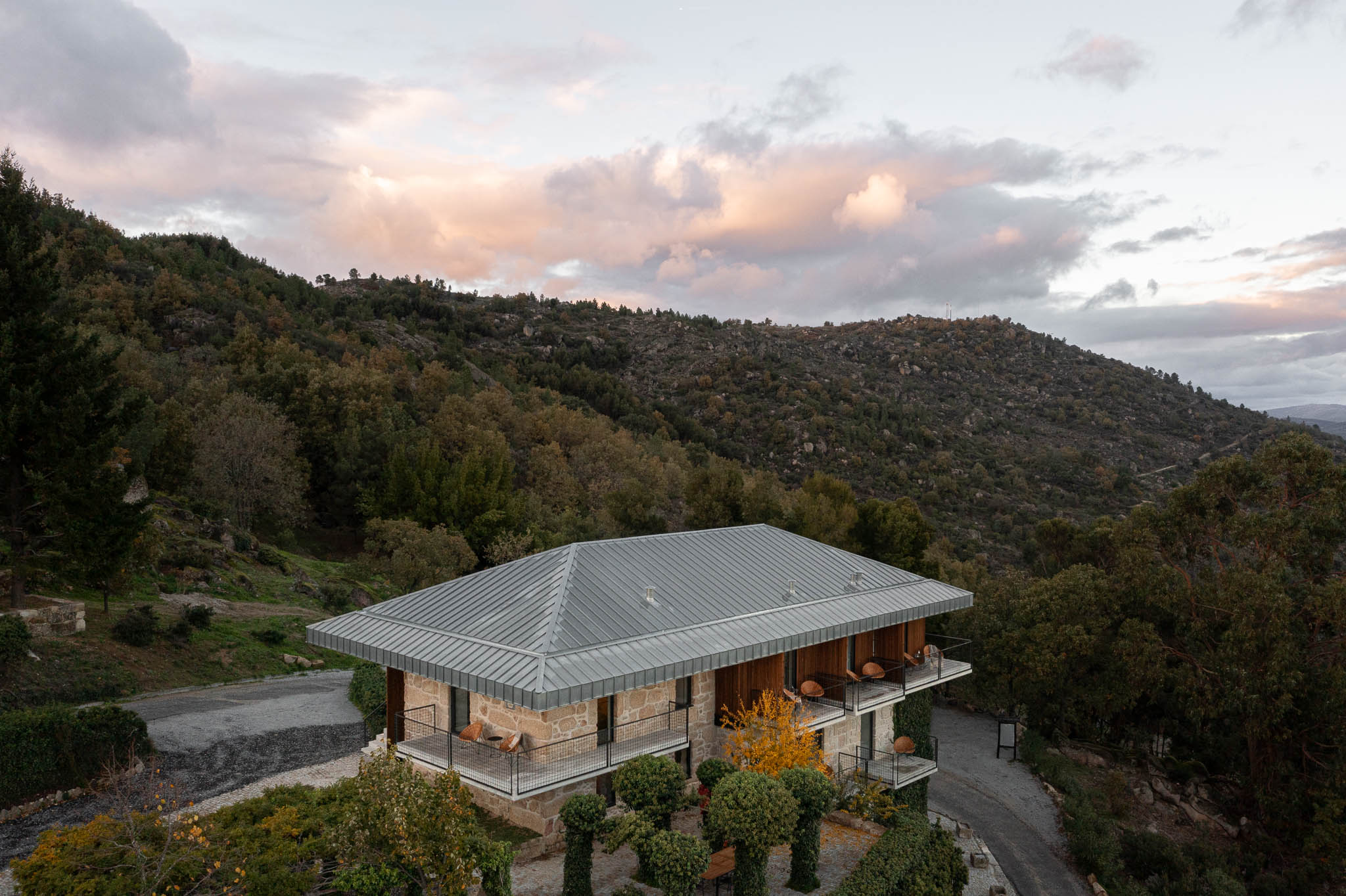 Exterior: Vista da casa de campo com telhado metálico e varandas, inserida na paisagem montanhosa. — The Vagar – Country House arquitetura David Bilo Arquitectos e Filipe Pina Arquitectura em Belmonte