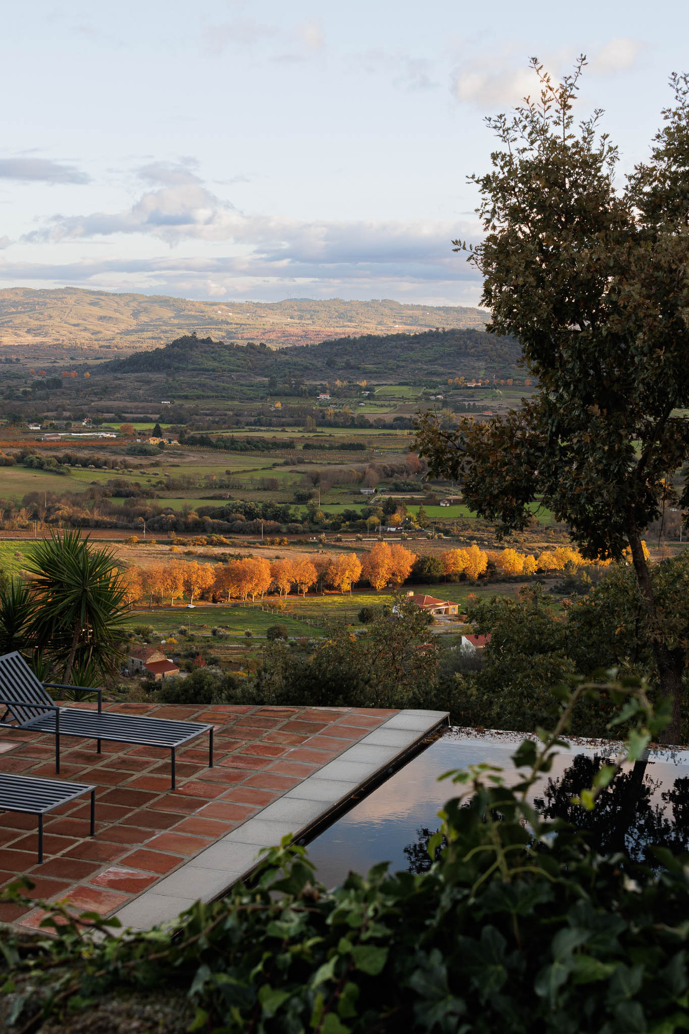 Piscina: Espreguiçadeiras junto à piscina com vista para a paisagem rural. Pavimento em tijoleira. — The Vagar – Country House arquitetura David Bilo Arquitectos e Filipe Pina Arquitectura em Belmonte