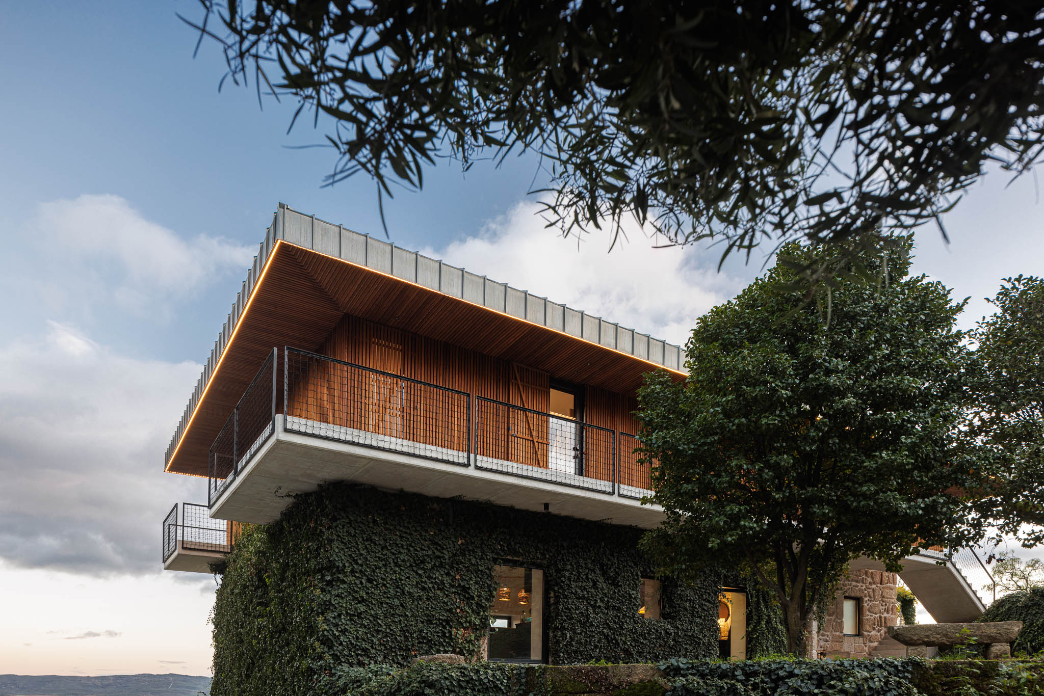 Exterior: Vista da casa de campo com iluminação exterior, revestimento em pedra e madeira. — The Vagar – Country House arquitetura David Bilo Arquitectos e Filipe Pina Arquitectura em Belmonte