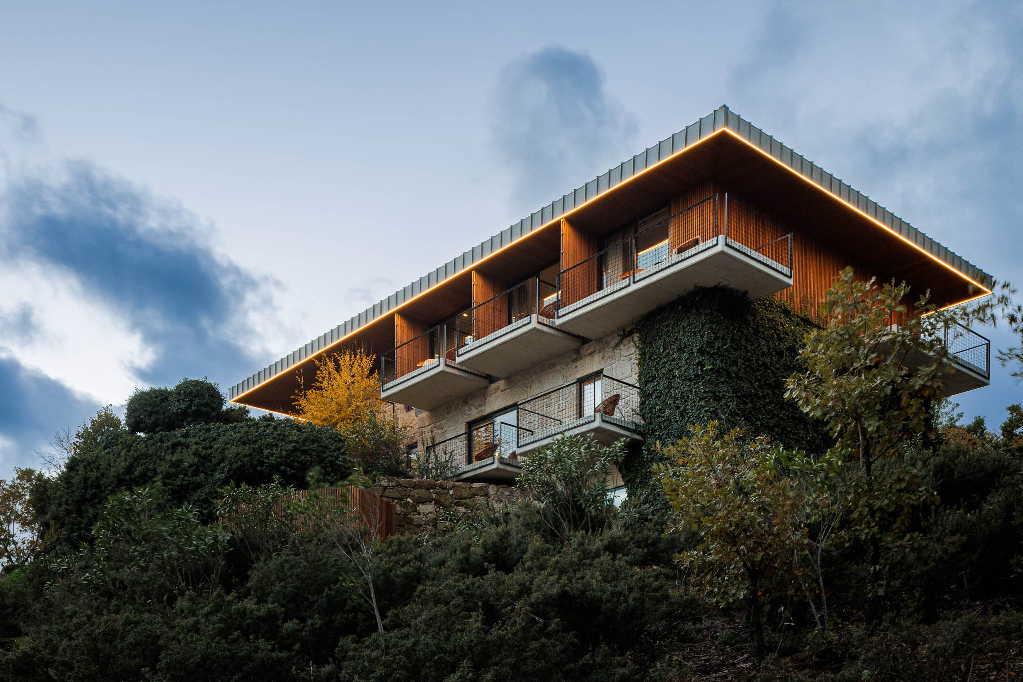 Exterior: Vista noturna da casa de campo com iluminação exterior, varandas e revestimento em pedra. — The Vagar – Country House arquitetura David Bilo Arquitectos e Filipe Pina Arquitectura em Belmonte