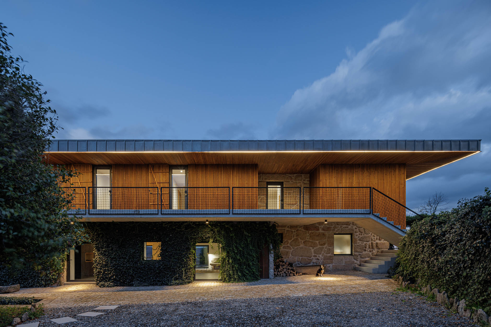 Exterior: Vista noturna da casa de campo com telhado metálico e iluminação exterior. — The Vagar – Country House arquitetura David Bilo Arquitectos e Filipe Pina Arquitectura em Belmonte