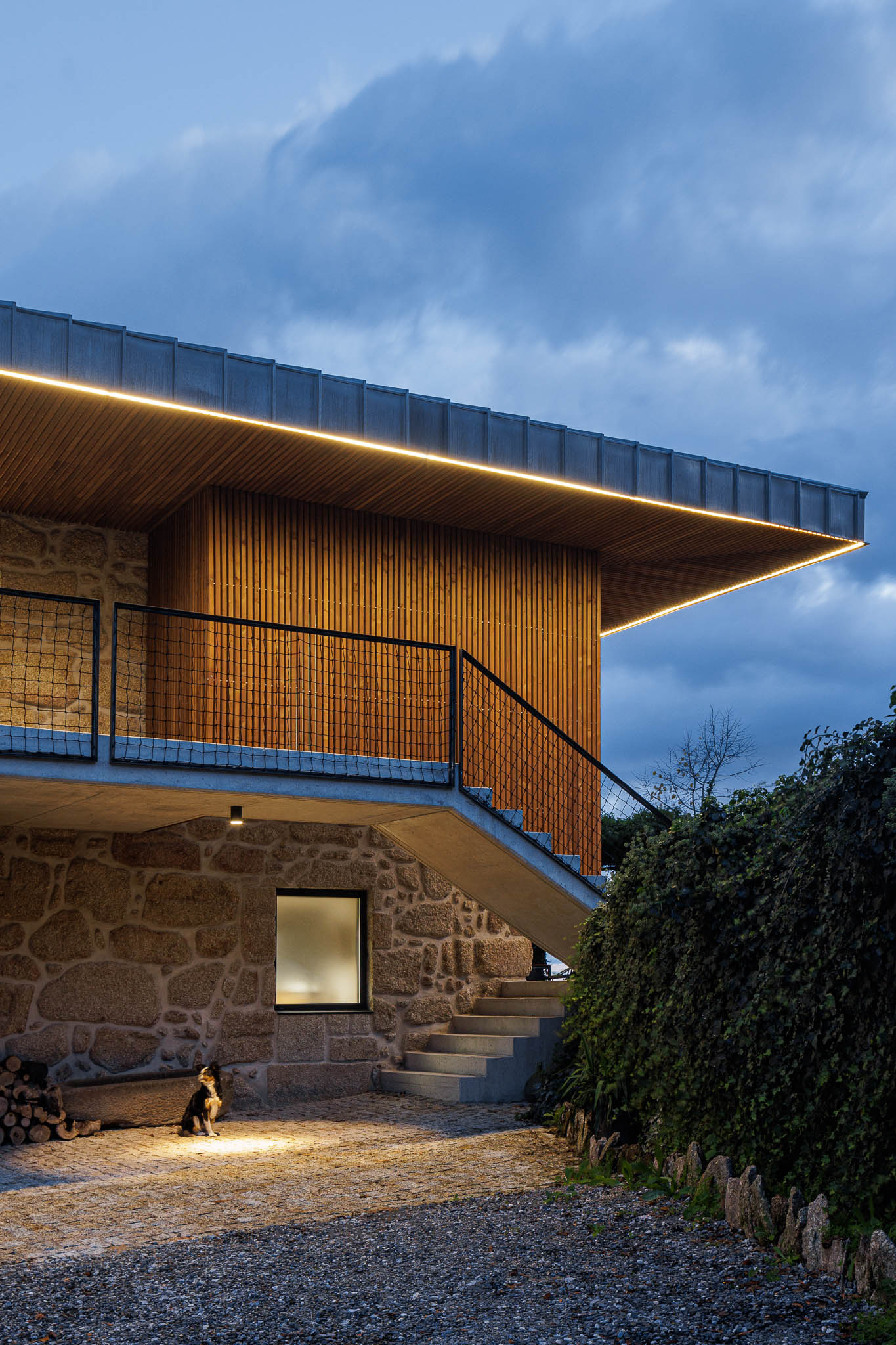 Exterior: Vista noturna da casa de campo com revestimento em pedra e escadas de acesso. — The Vagar – Country House arquitetura David Bilo Arquitectos e Filipe Pina Arquitectura em Belmonte