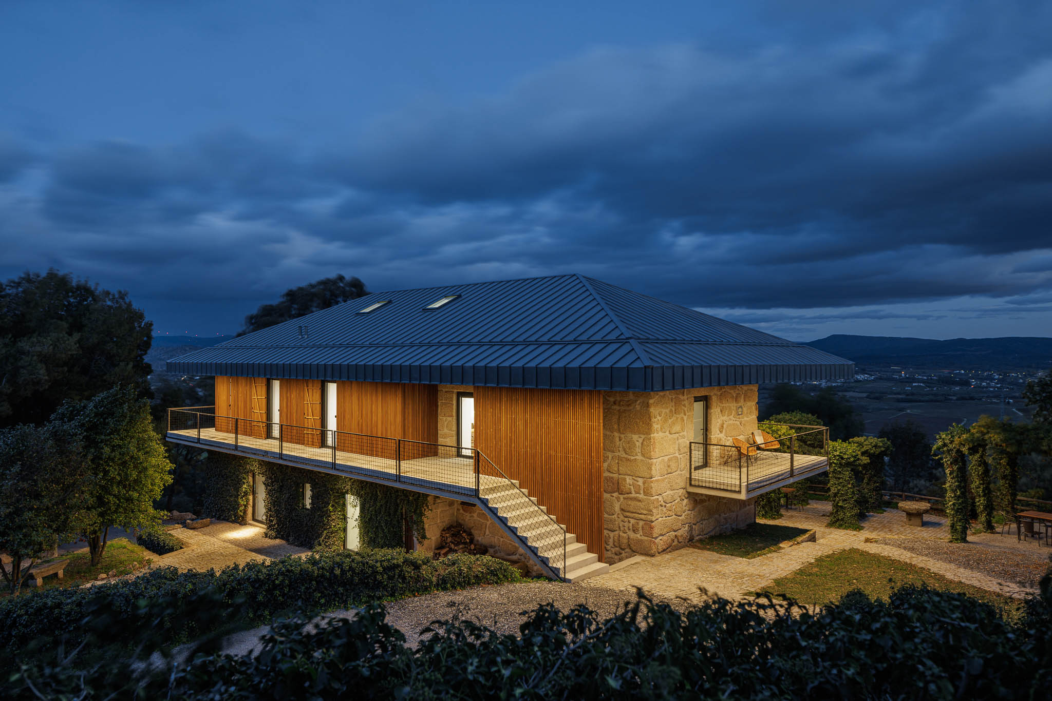 Exterior: Vista noturna da casa de campo com varandas e escadas de acesso. — The Vagar – Country House arquitetura David Bilo Arquitectos e Filipe Pina Arquitectura em Belmonte