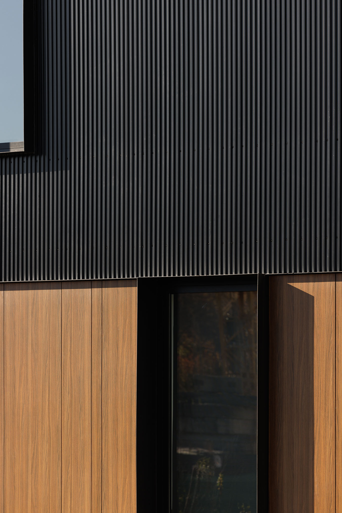 Fachada: Detalhe de revestimento exterior em madeira e metal preto, com porta envidraçada. — Clínica de fisioterapia - Fisiminho arquitetura L2C Arquitetura em Braga