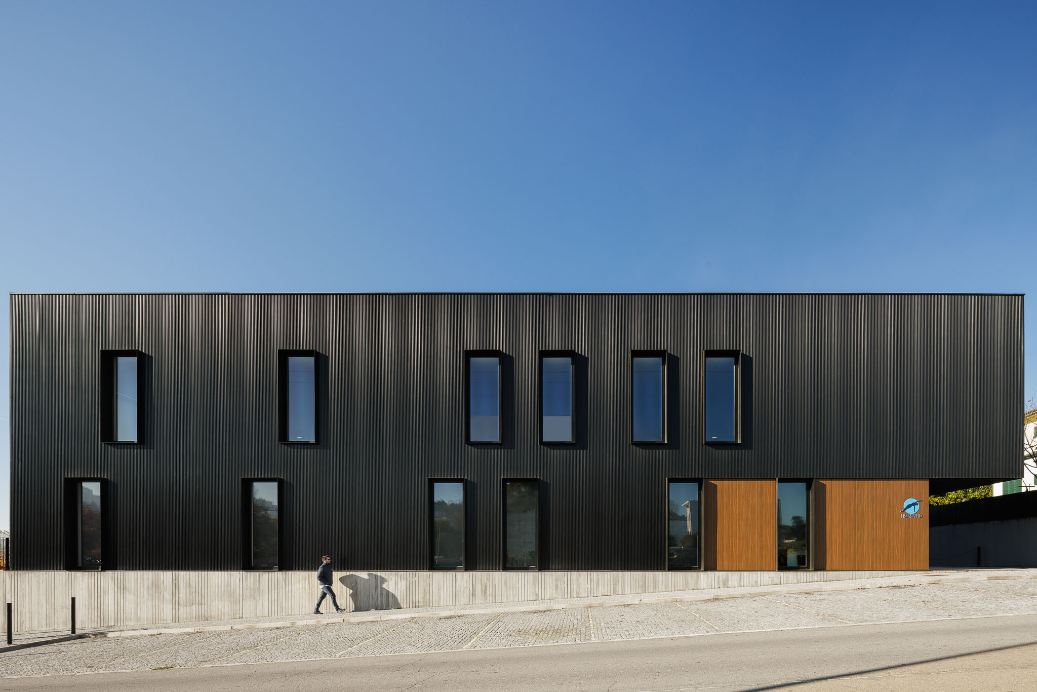 Fachada: Edifício com revestimento metálico preto, janelas retangulares e base em betão aparente. — Clínica de fisioterapia - Fisiminho arquitetura L2C Arquitetura em Braga
