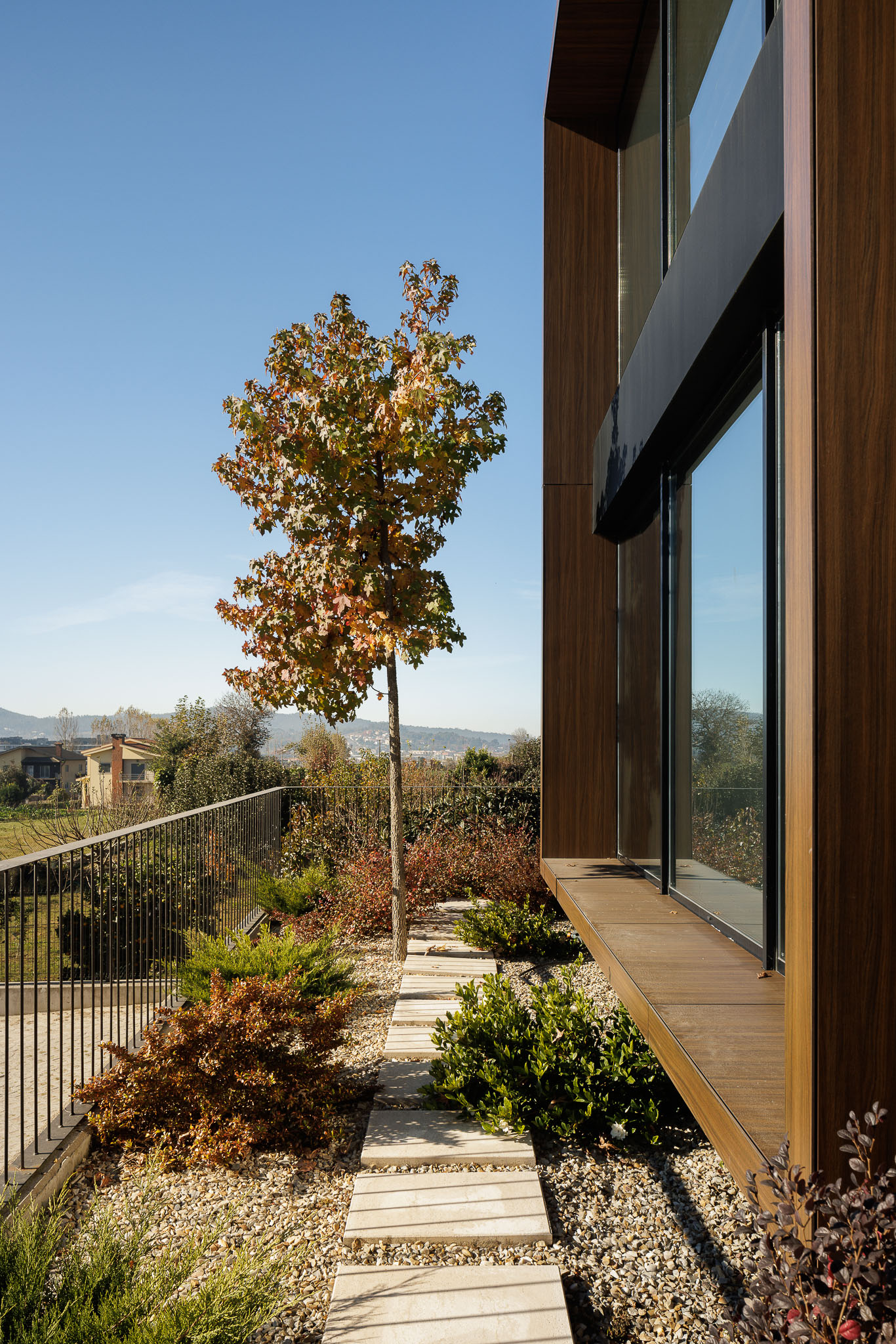 Exterior: Caminho em lajes de pedra num jardim com arbustos, junto a fachada em madeira. — Clínica de fisioterapia - Fisiminho arquitetura L2C Arquitetura em Braga