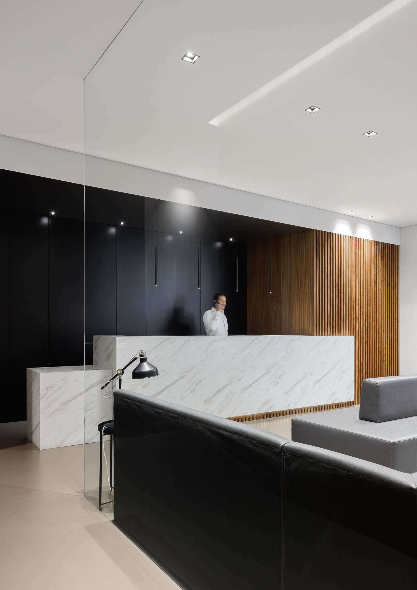 Recepção: Balcão em mármore branco, parede preta e revestimento em madeira vertical. — Clínica de fisioterapia - Fisiminho arquitetura L2C Arquitetura em Braga